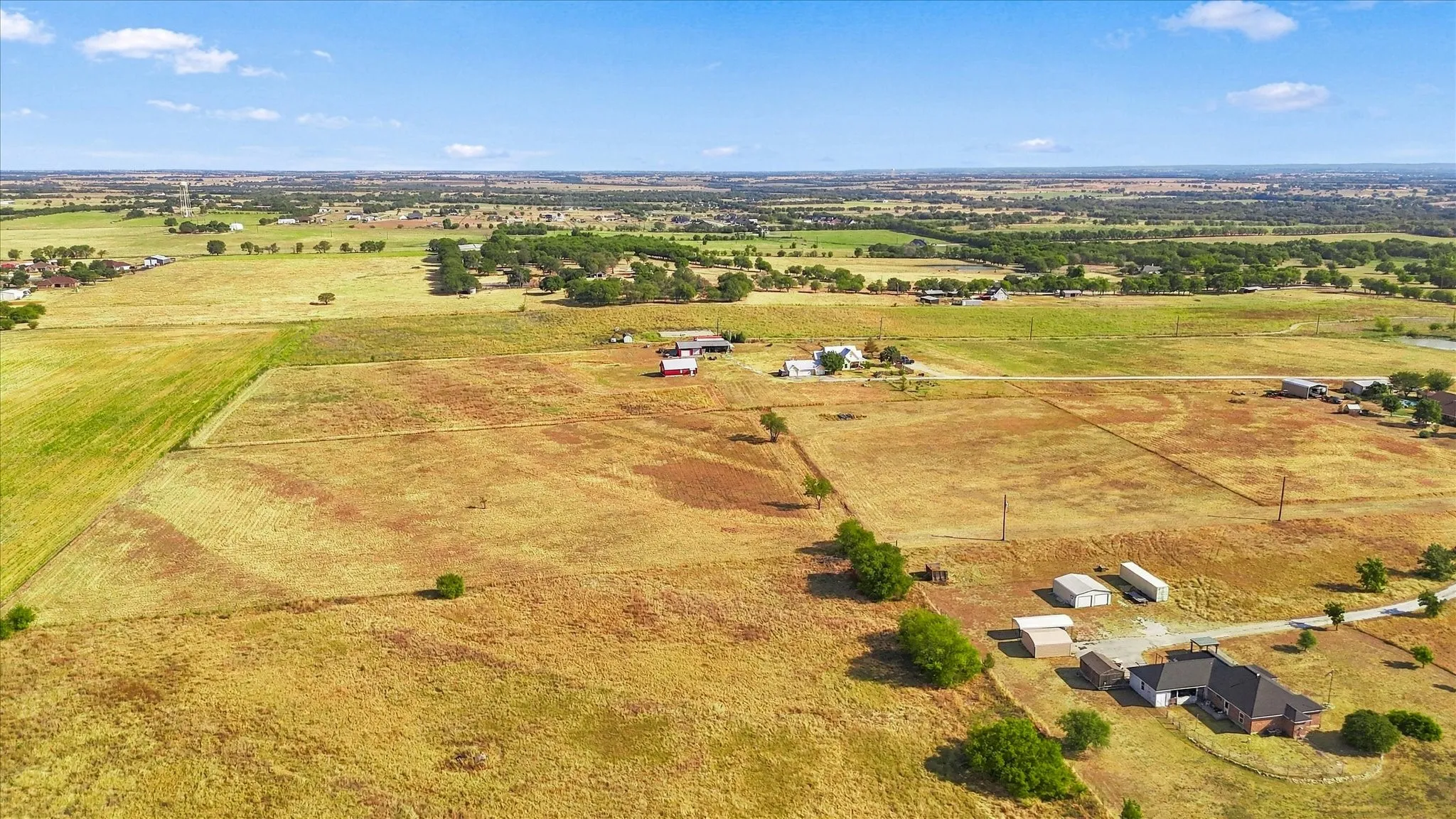 Expansive rural landscape featuring multiple parcels of open land, scattered trees, and distant residential structures