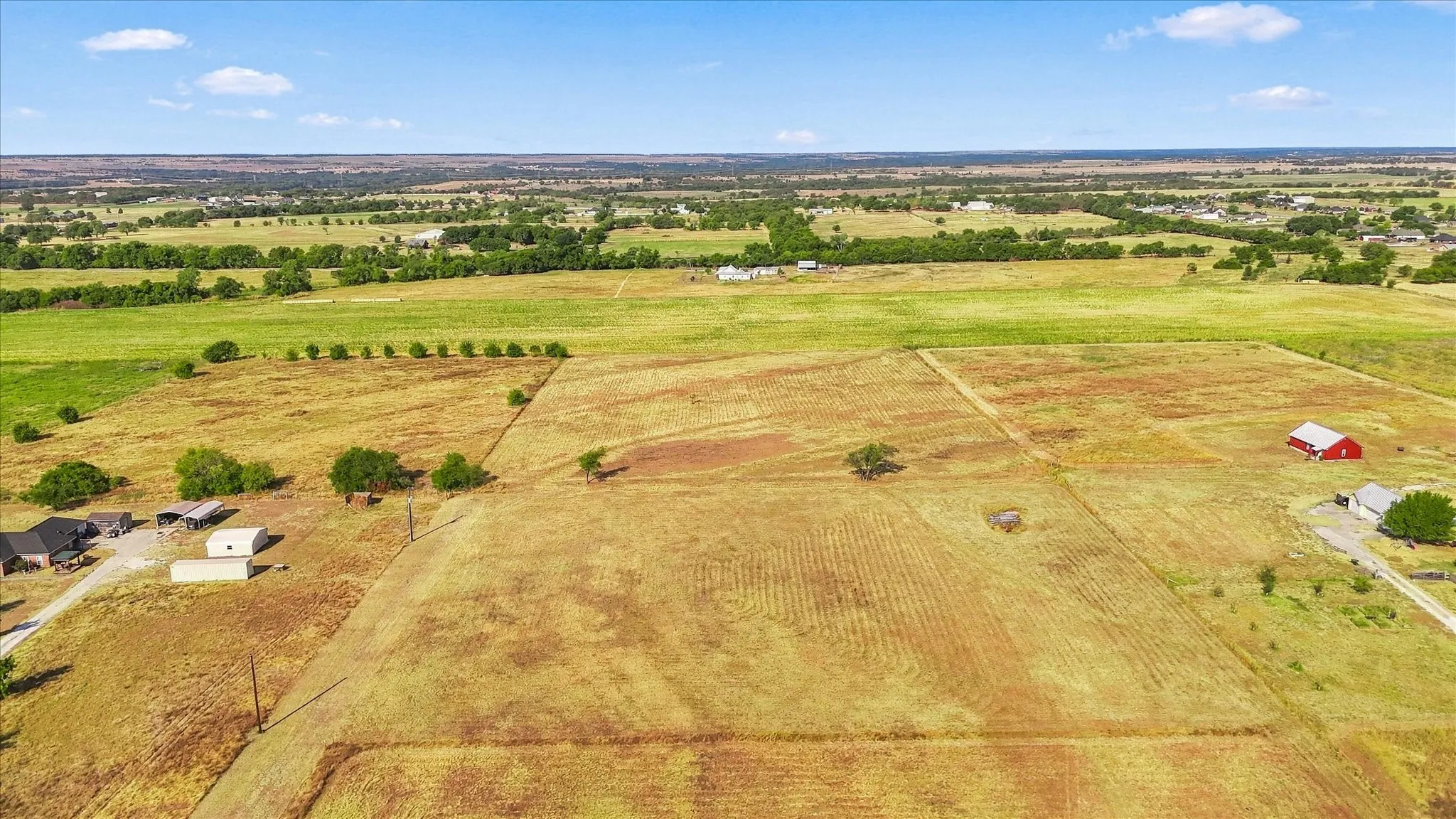 Expansive agricultural land featuring a red barn, scattered trees, and distant green pastures