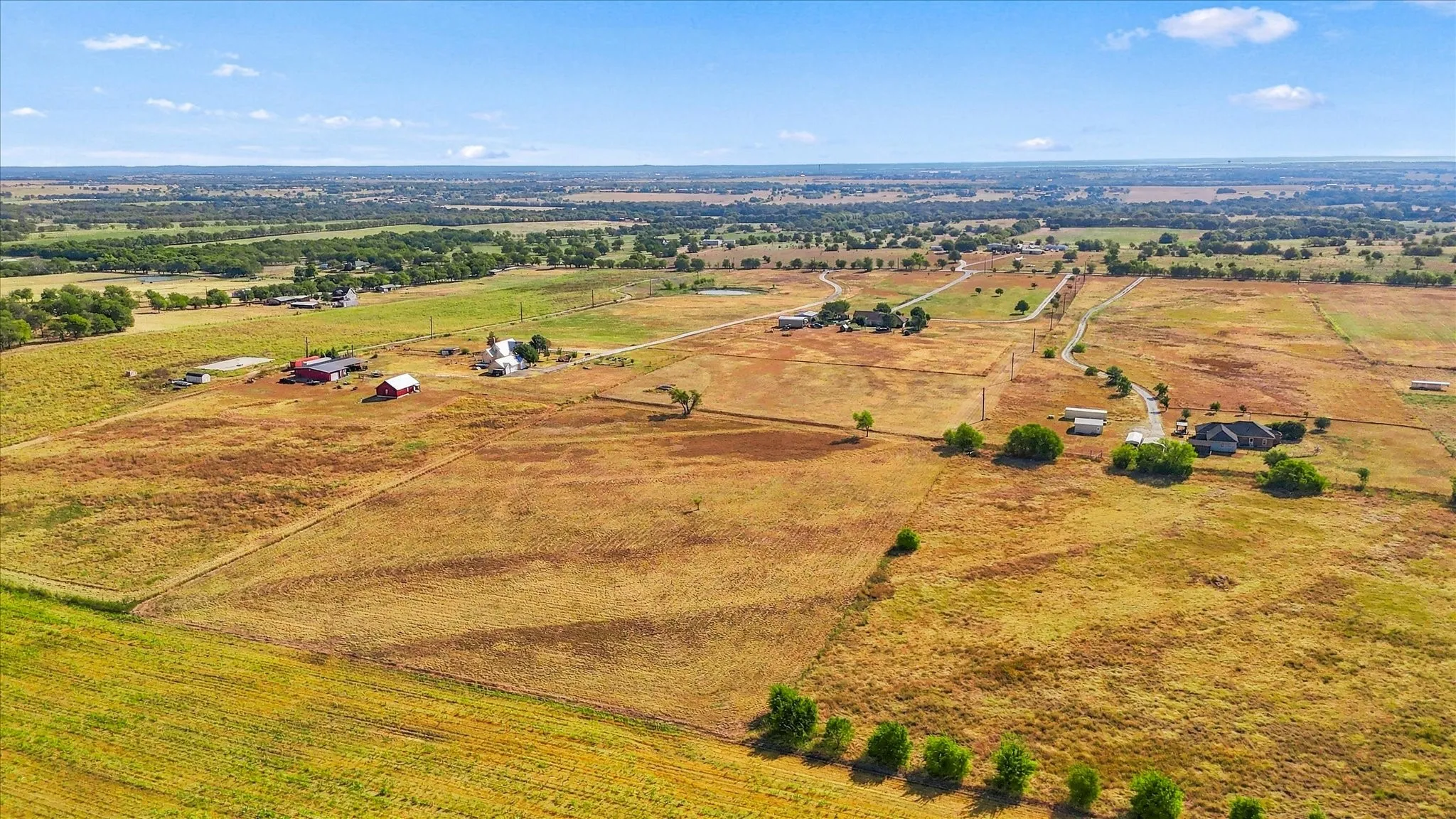 Expansive acreage featuring multiple structures, open fields, and distant tree lines under a clear sky