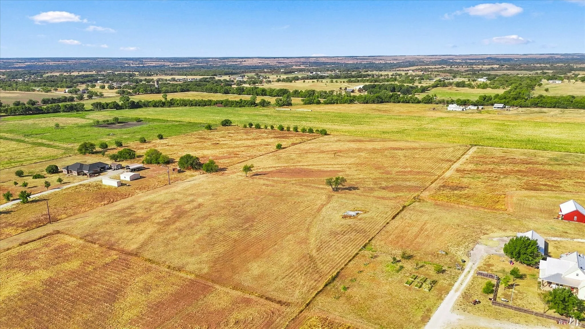 Expansive acreage with open fields, scattered mature trees, and distant structures