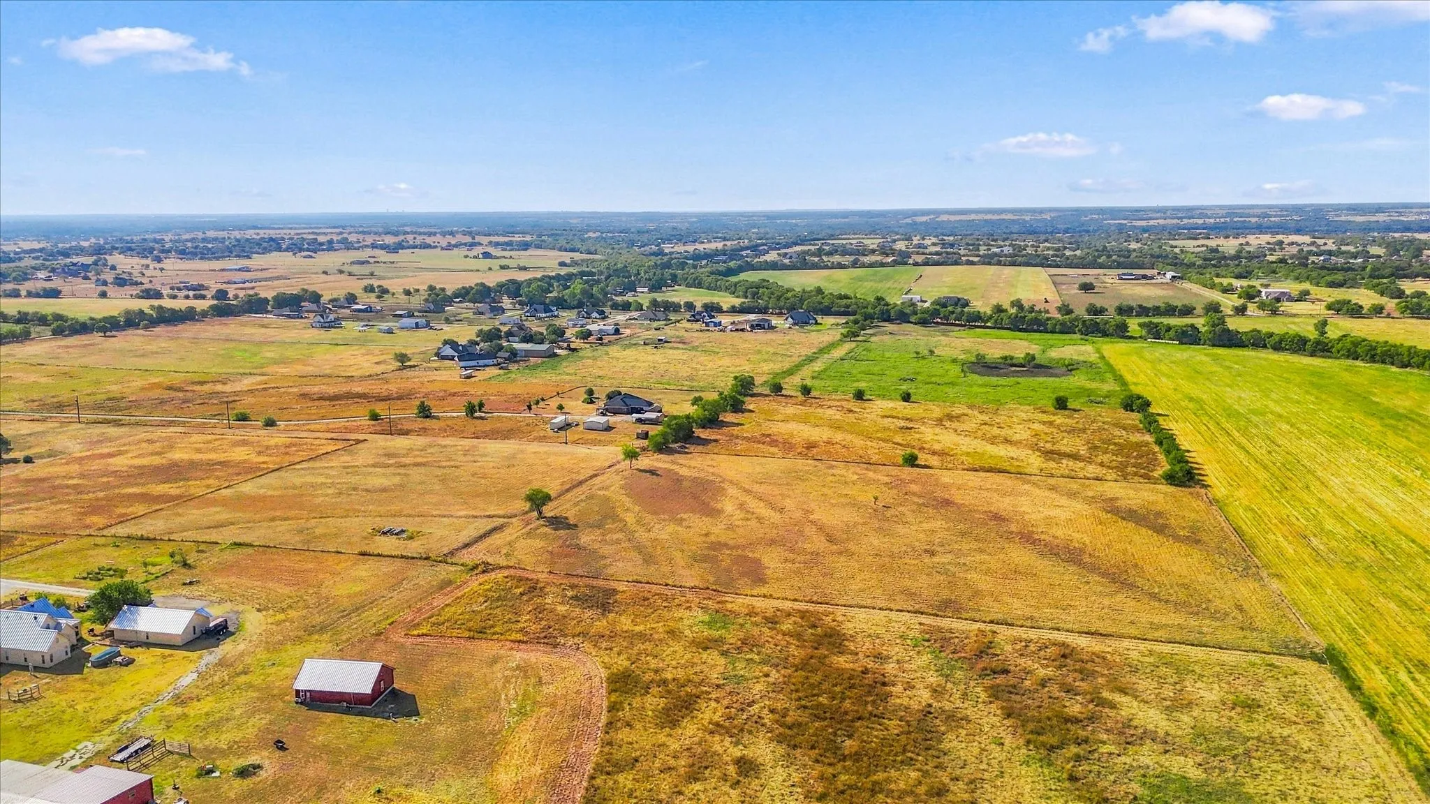 Expansive rural landscape featuring open fields, scattered residential structures, and distant foliage