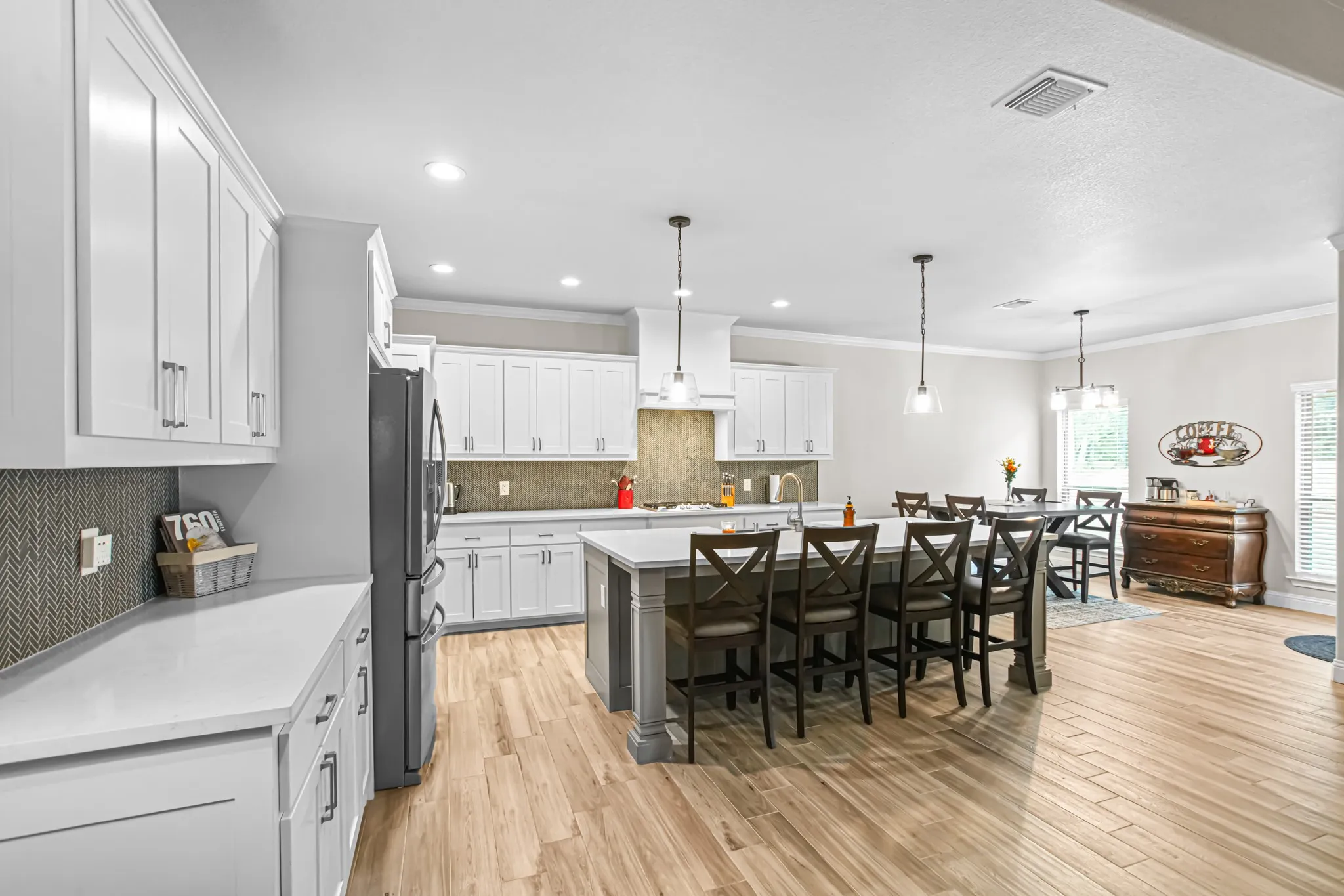 Kitchen featuring white cabinetry, light-toned wood-finish flooring, a central island with seating, pendant lighting, and stainless steel appliances