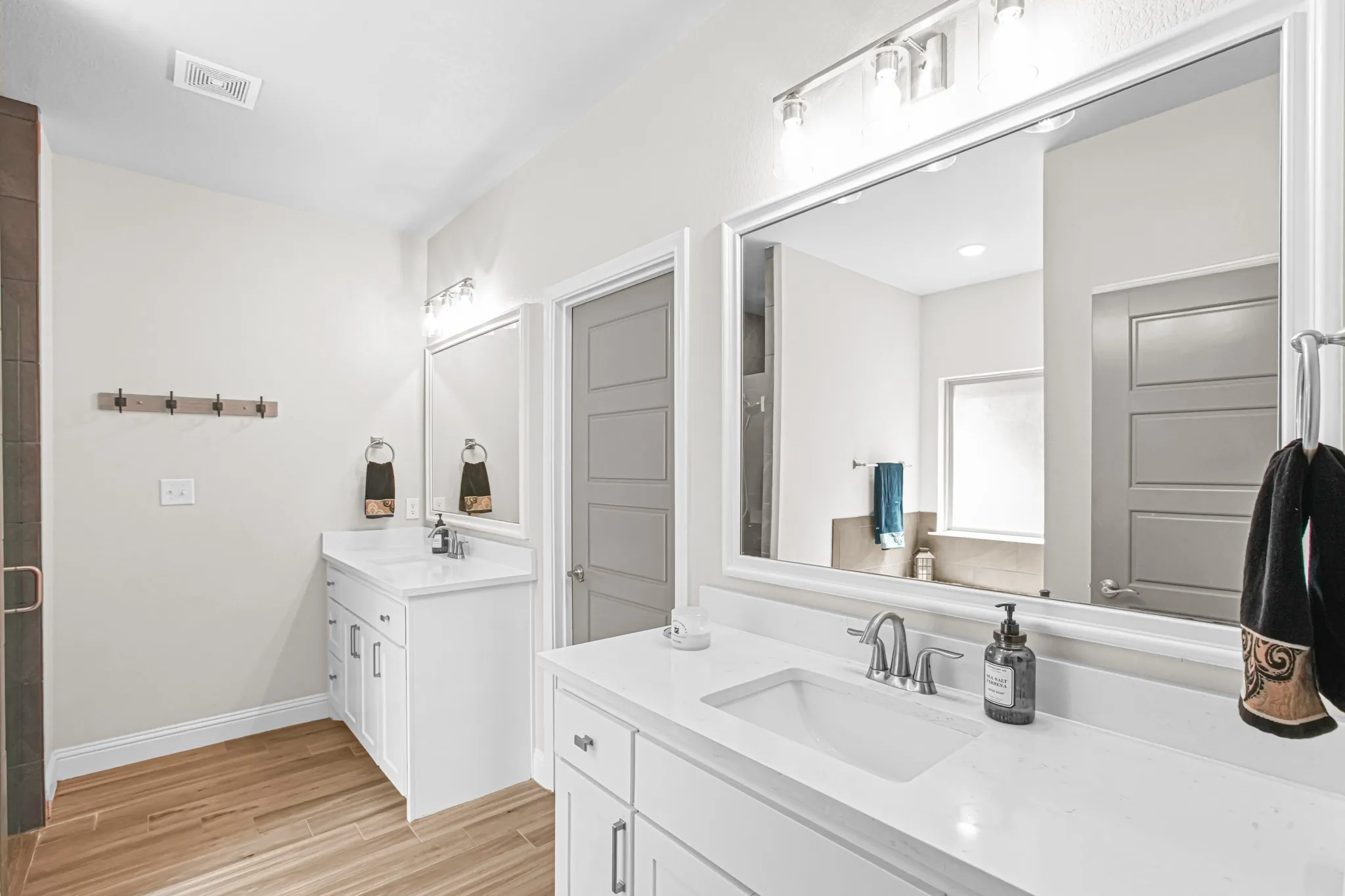 Dual vanities with white cabinetry and integrated sinks, wood-finish flooring, large framed mirror, and track lighting fixtures