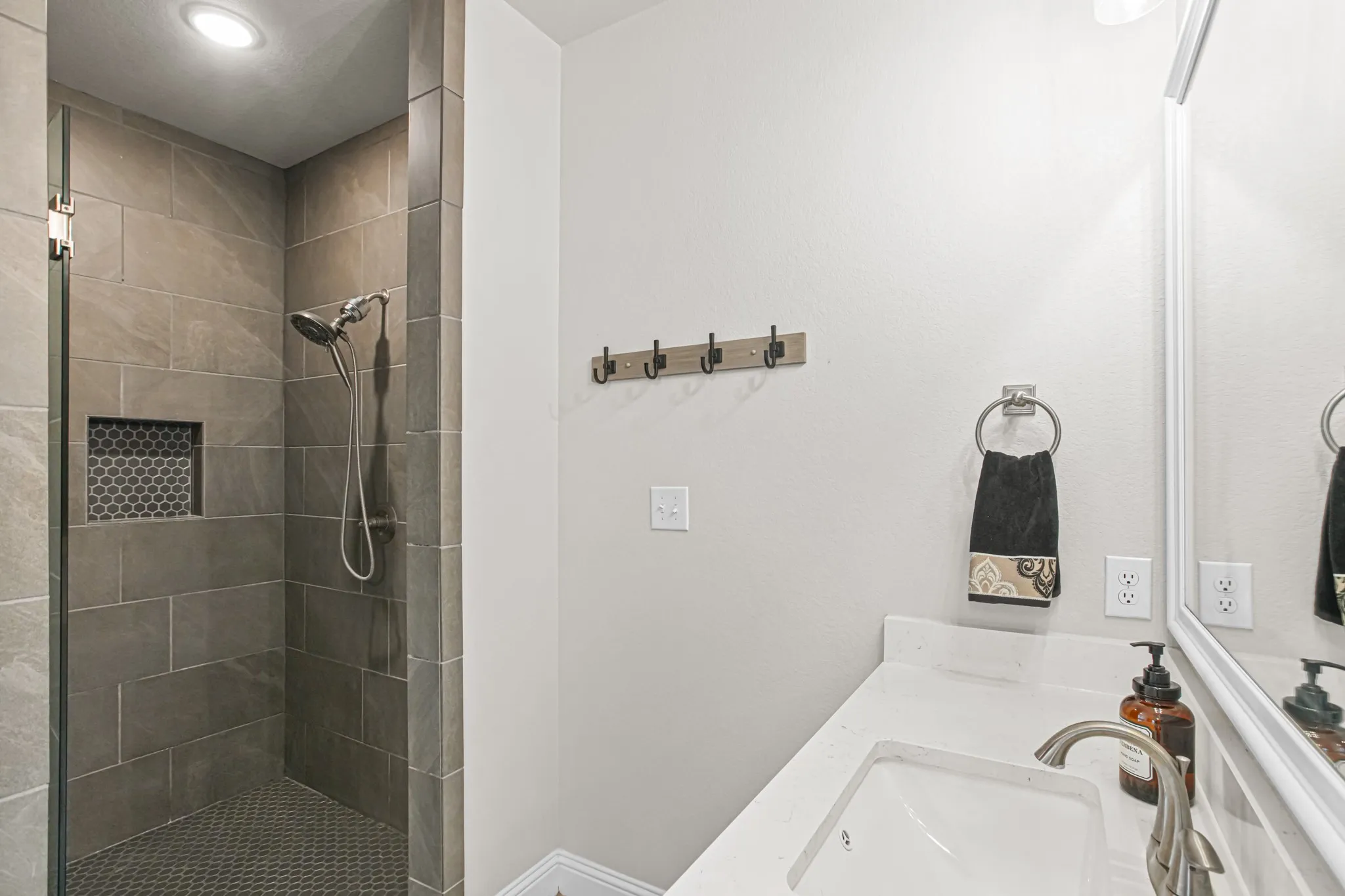 Walk-in shower with tile surround, built-in shower niche with mosaic tile accent, and a handheld showerhead