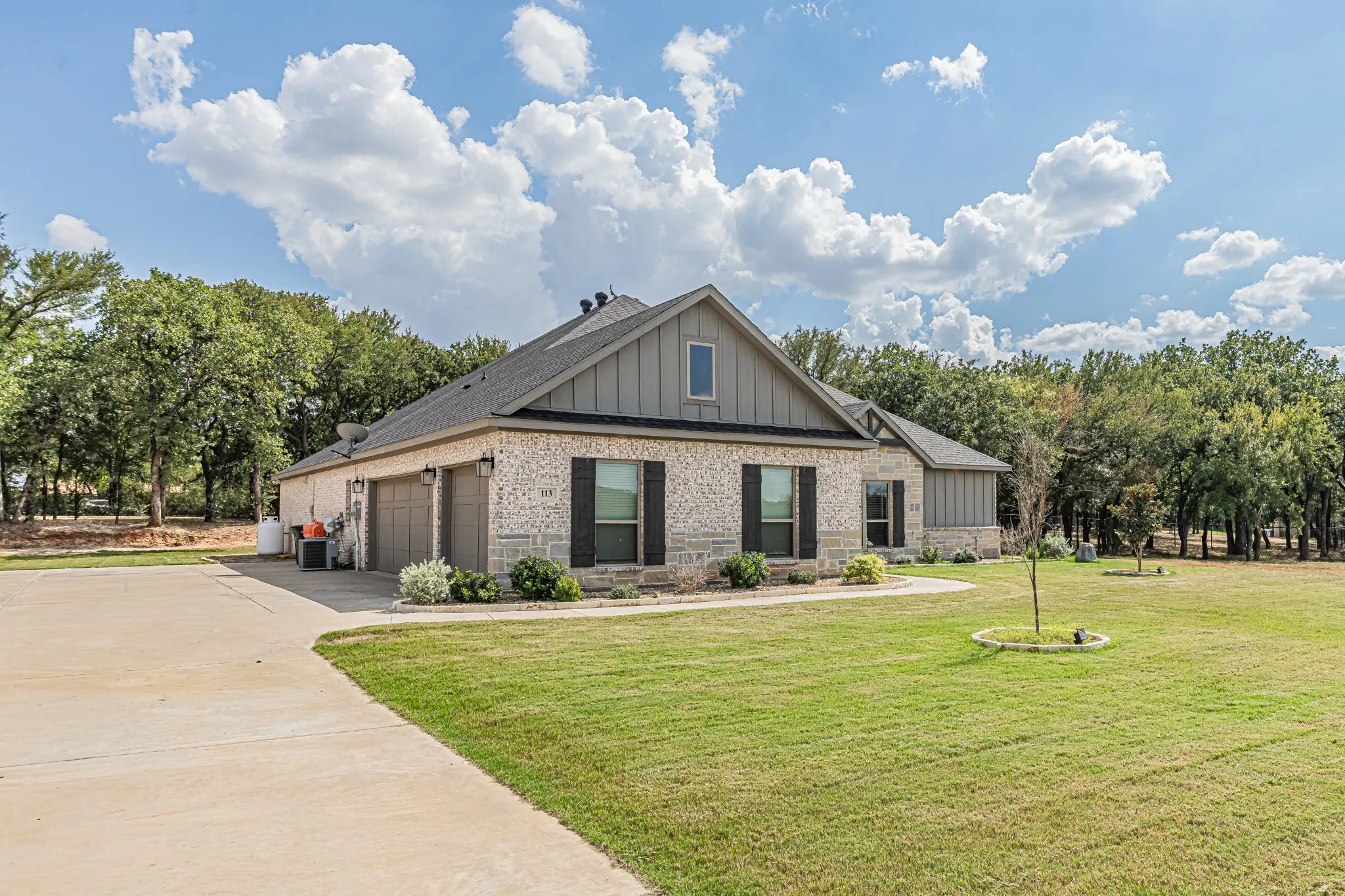 Stone facade with vertical siding accents, two-car garage, concrete driveway, front landscaping, and expansive green lawn