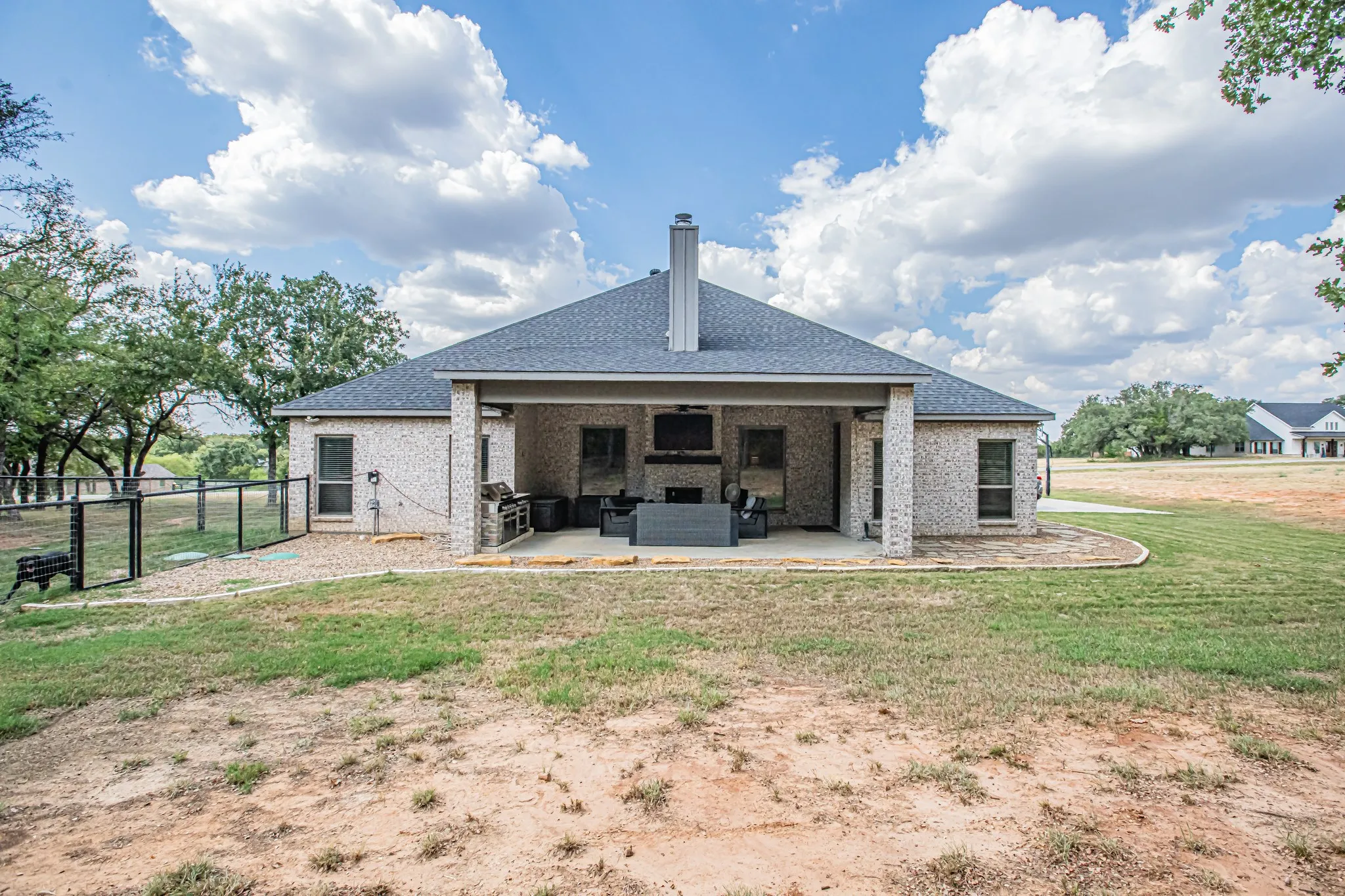 Covered patio with brick columns, an outdoor fireplace, a built-in outdoor grill area, and a fenced pet enclosure