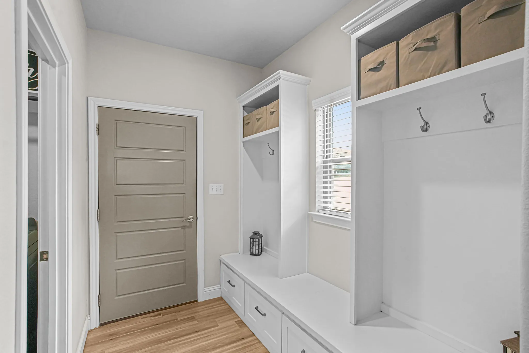 Built-in storage bench with drawers, white cabinetry, wood-finish flooring, and natural light from a window with blinds