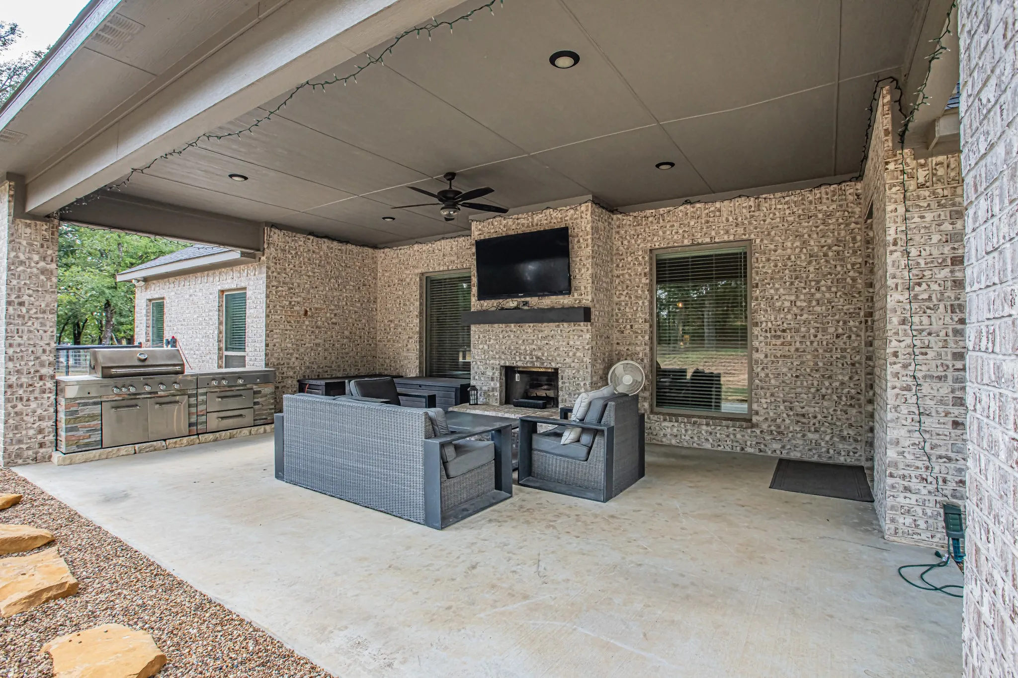 Expansive covered patio featuring a built-in outdoor kitchen, stone fireplace, recessed lighting, and a ceiling fan