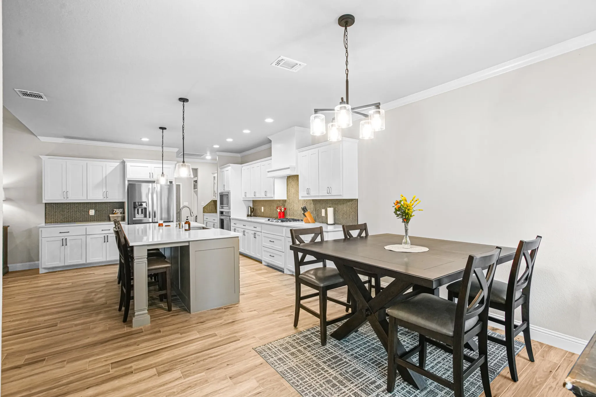 Open-concept kitchen and dining area featuring light wood-finish flooring, white cabinetry, a large kitchen island with counter seating, stainless steel appliances, and recessed lighting