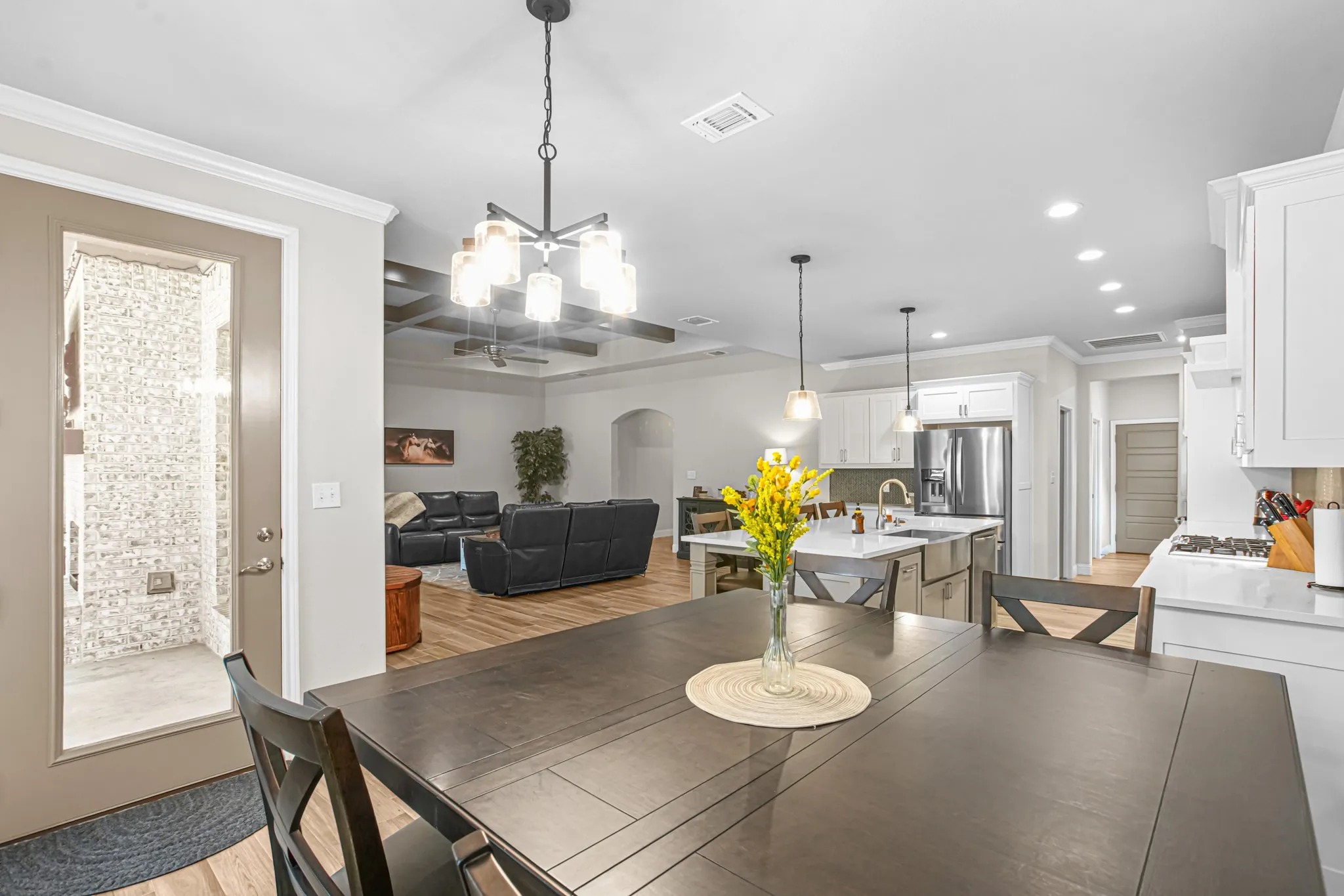 Open-concept living area featuring wood-finish flooring, a kitchen island with pendant lighting, and a stainless steel refrigerator