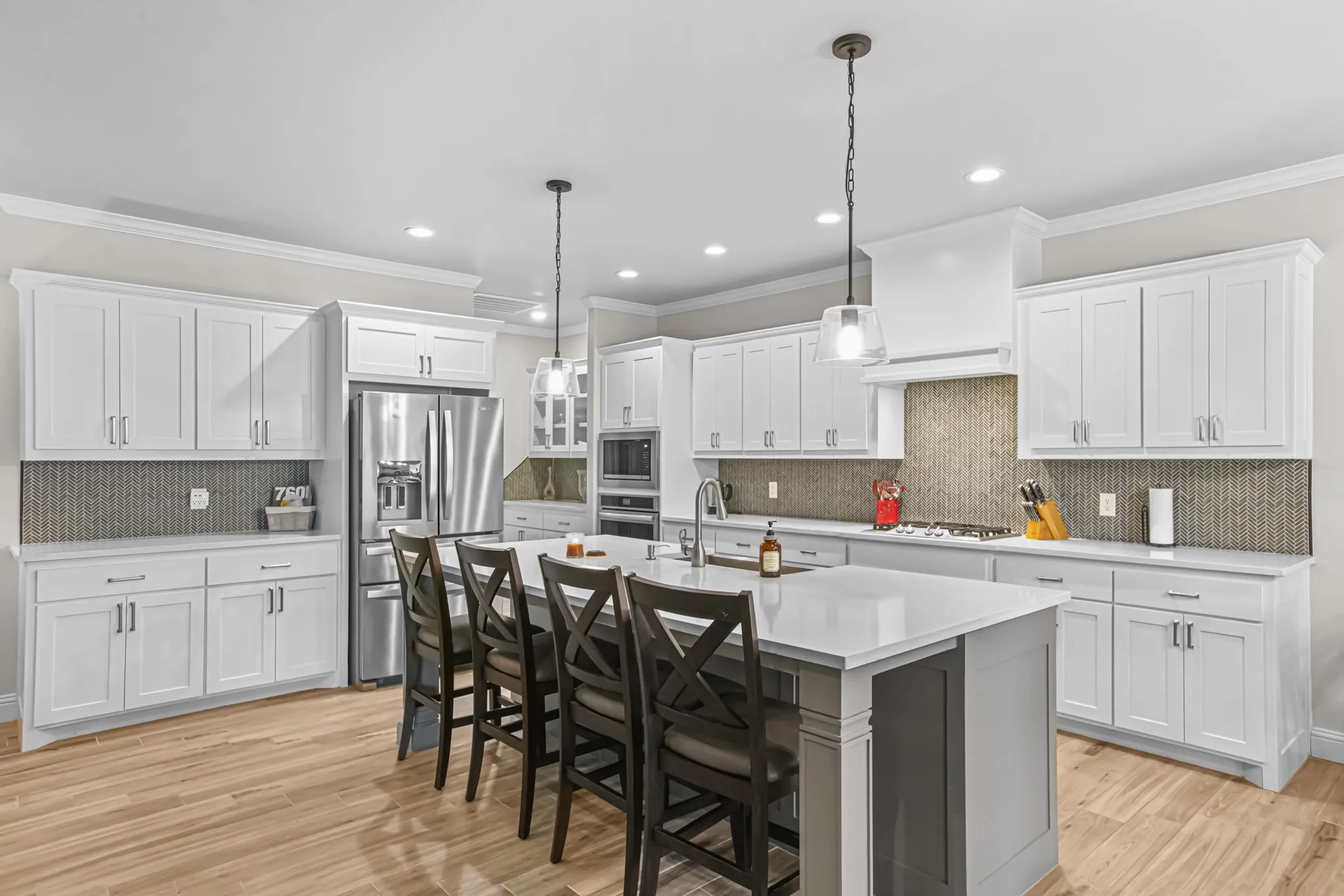White cabinetry, stainless steel appliances, wood-finish flooring, central island with seating, and mosaic tile backsplash