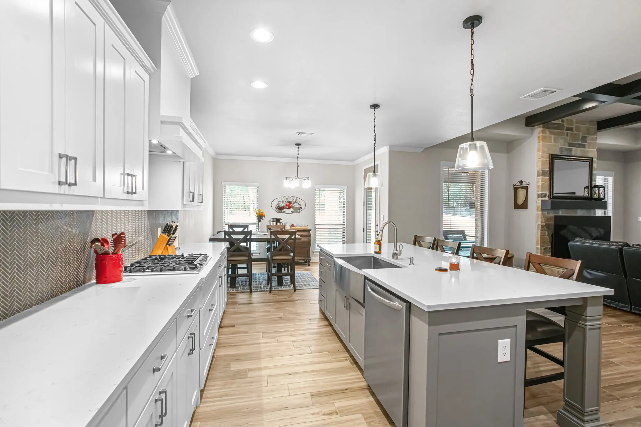 Kitchen featuring white shaker-style cabinetry, a herringbone tile backsplash, white countertops, wood-finish flooring, and a central island with an integrated sink
