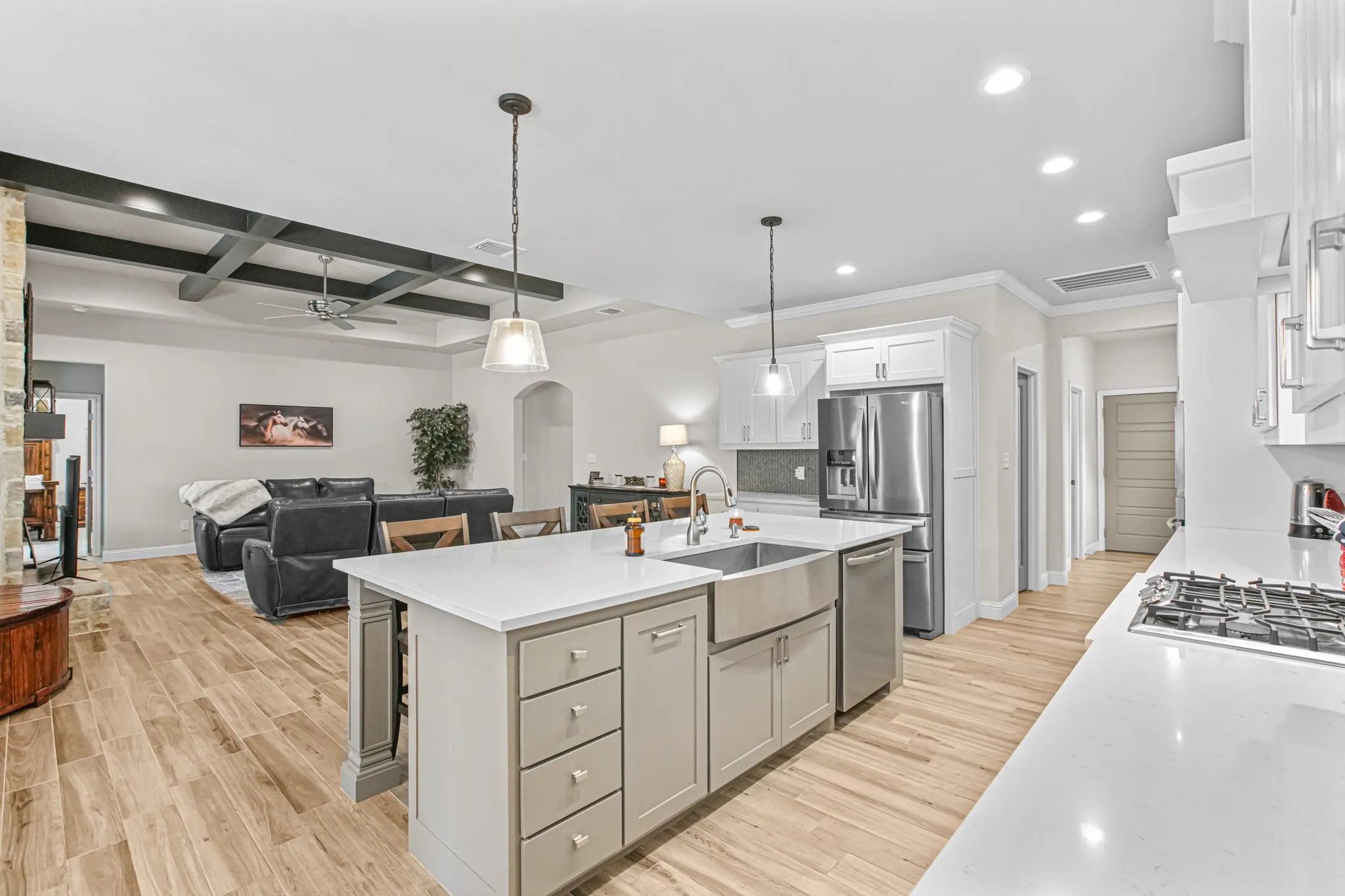 Open-concept living space with wood-finish flooring, kitchen island with built-in sink, stainless steel appliances, and coffered ceilings