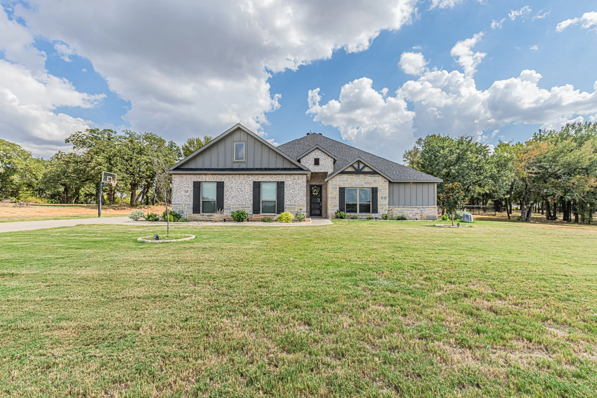 Stone and siding exterior with dark shutters, gabled roofline, and established landscaping