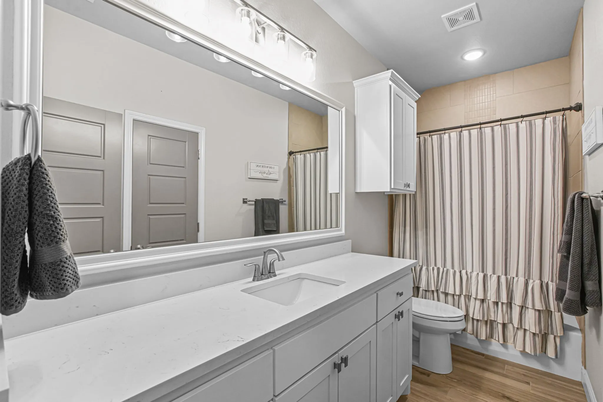 Extended vanity with integrated sink, brushed nickel faucet, large framed mirror, and wood-finish flooring