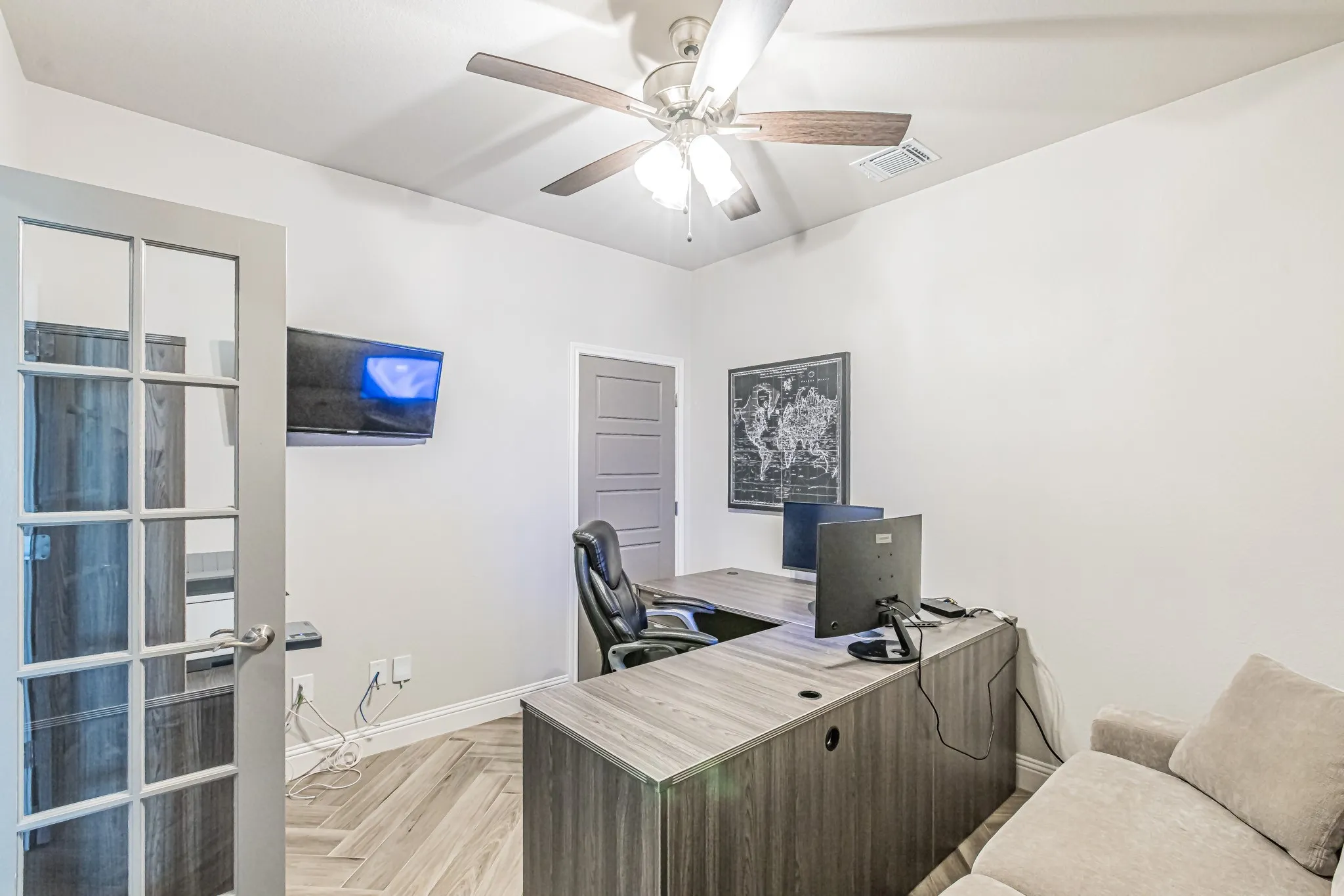 French doors with glass panes, wood-finish herringbone flooring, ceiling fan with light fixture, and a built-in wood-finish desk