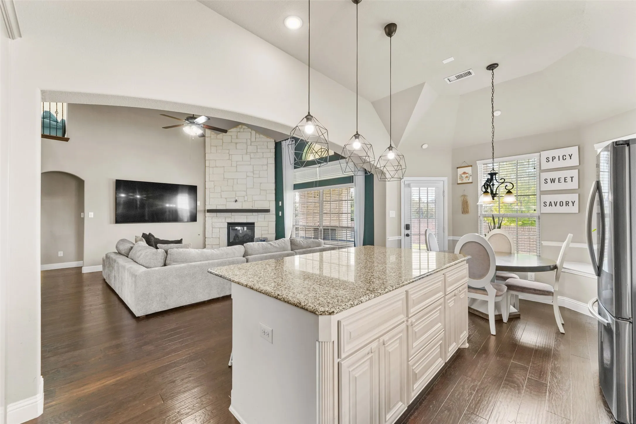 Spacious interior featuring a large kitchen island with a light-toned countertop, wood-finish flooring, a stone fireplace, and vaulted ceilings