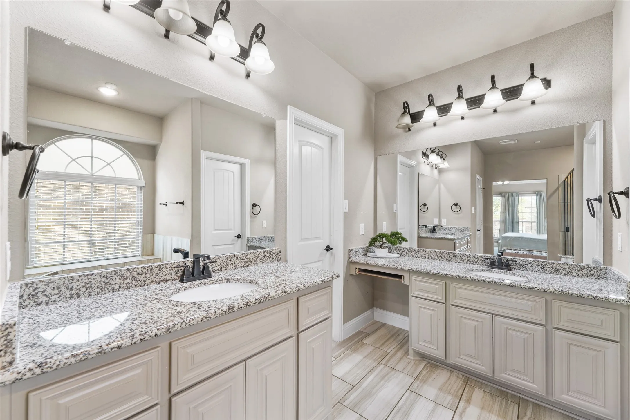 Dual vanity with light-toned cabinetry and stone-finish countertops, undermount sinks, and dark-finish fixtures