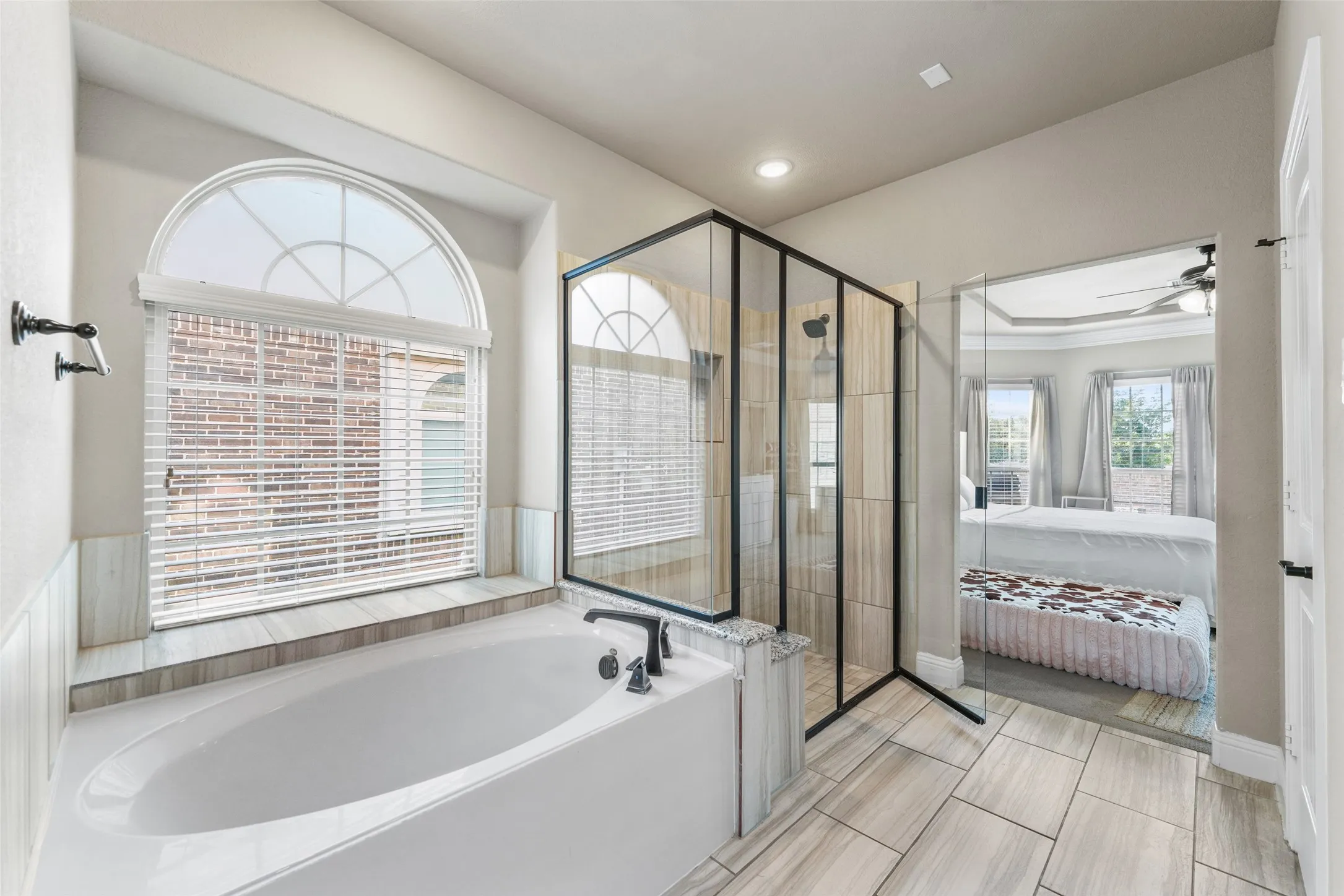 Soaking tub with a tile surround, arched window, and separate glass-enclosed shower