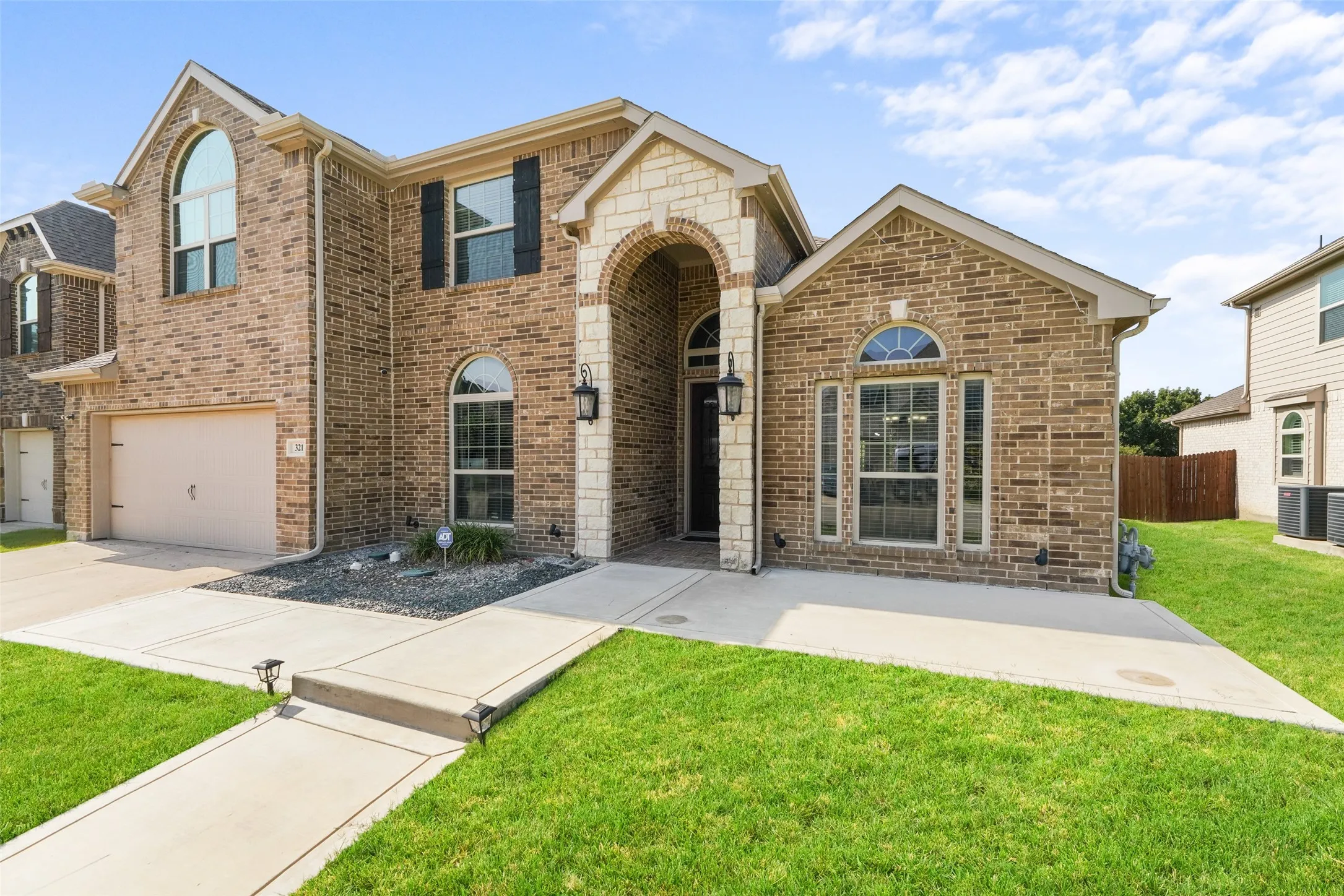 Brick and stone exterior with arched windows, a two-car garage, and a concrete pathway