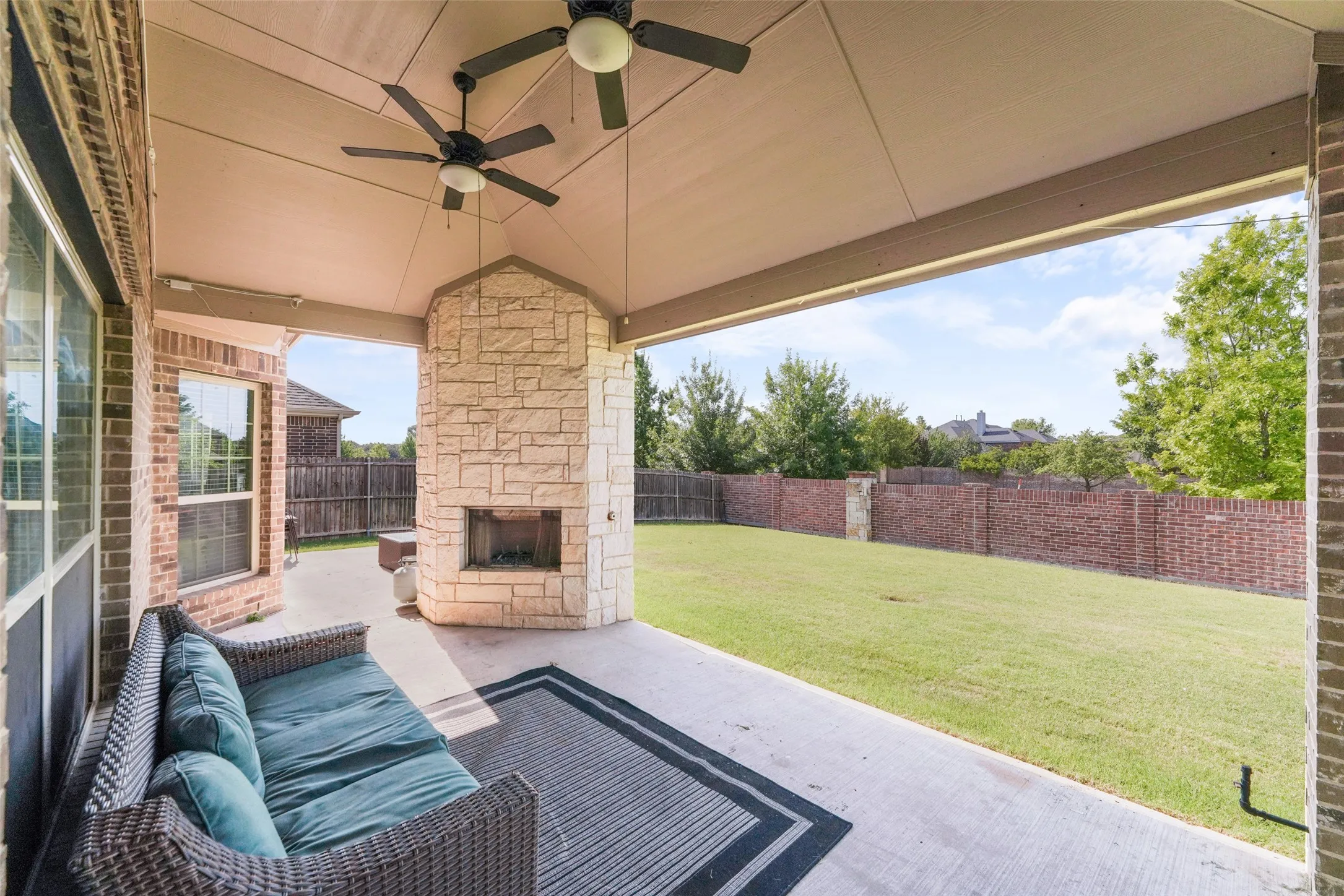 Covered patio with a stone-clad fireplace and two ceiling fans
