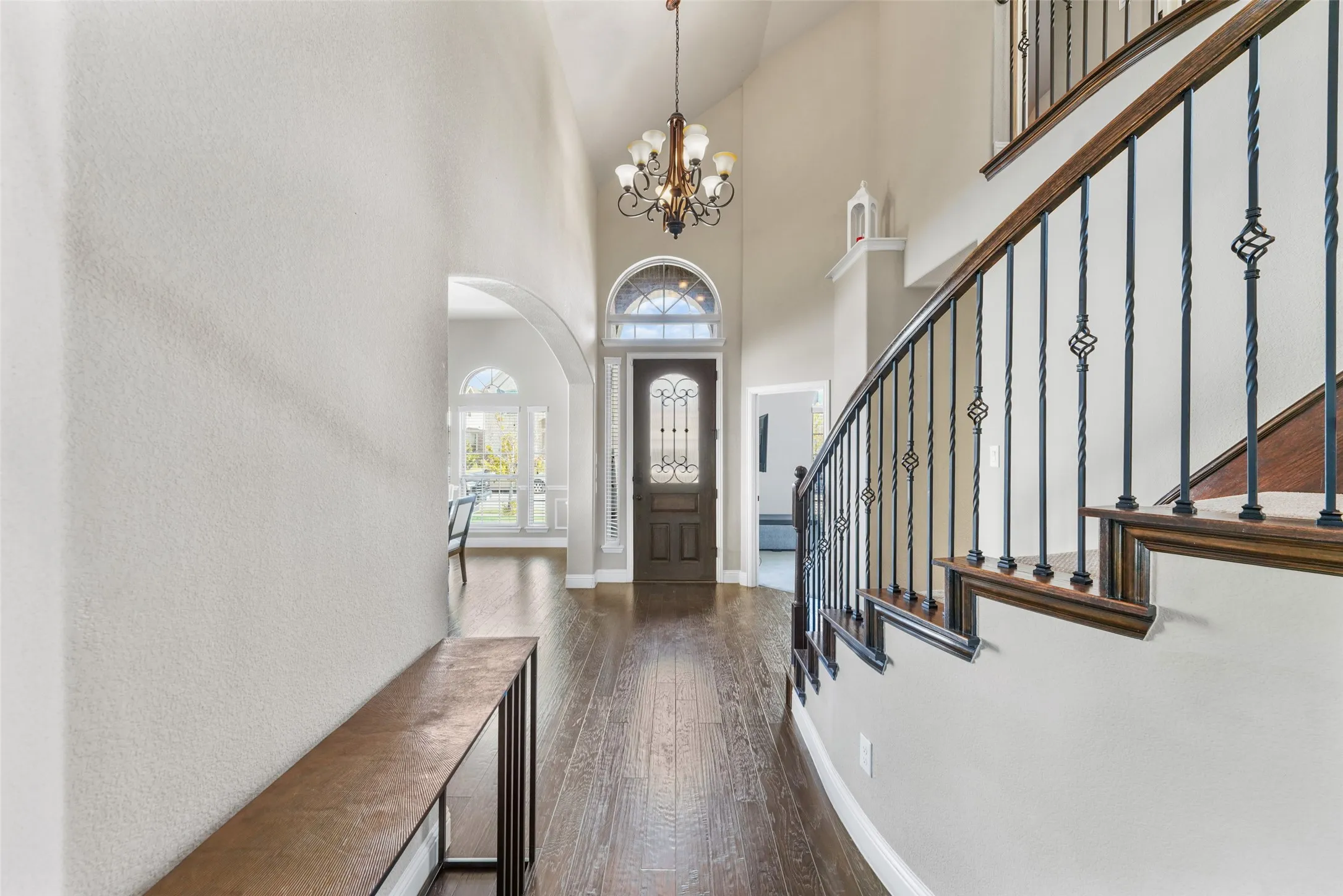 Two-story foyer with wood-finish flooring, a grand staircase featuring wrought iron balusters, a vaulted ceiling, and an arched entryway