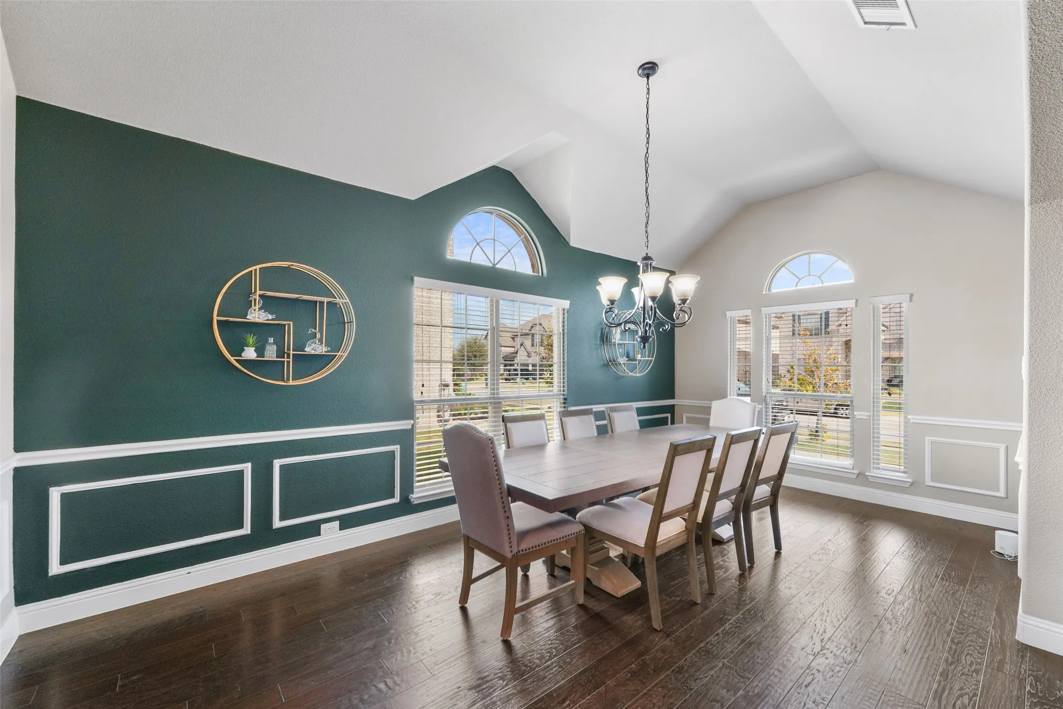 Vaulted ceiling with an elegant chandelier, wood-finish flooring, accent wall with wainscoting, and arched transom windows