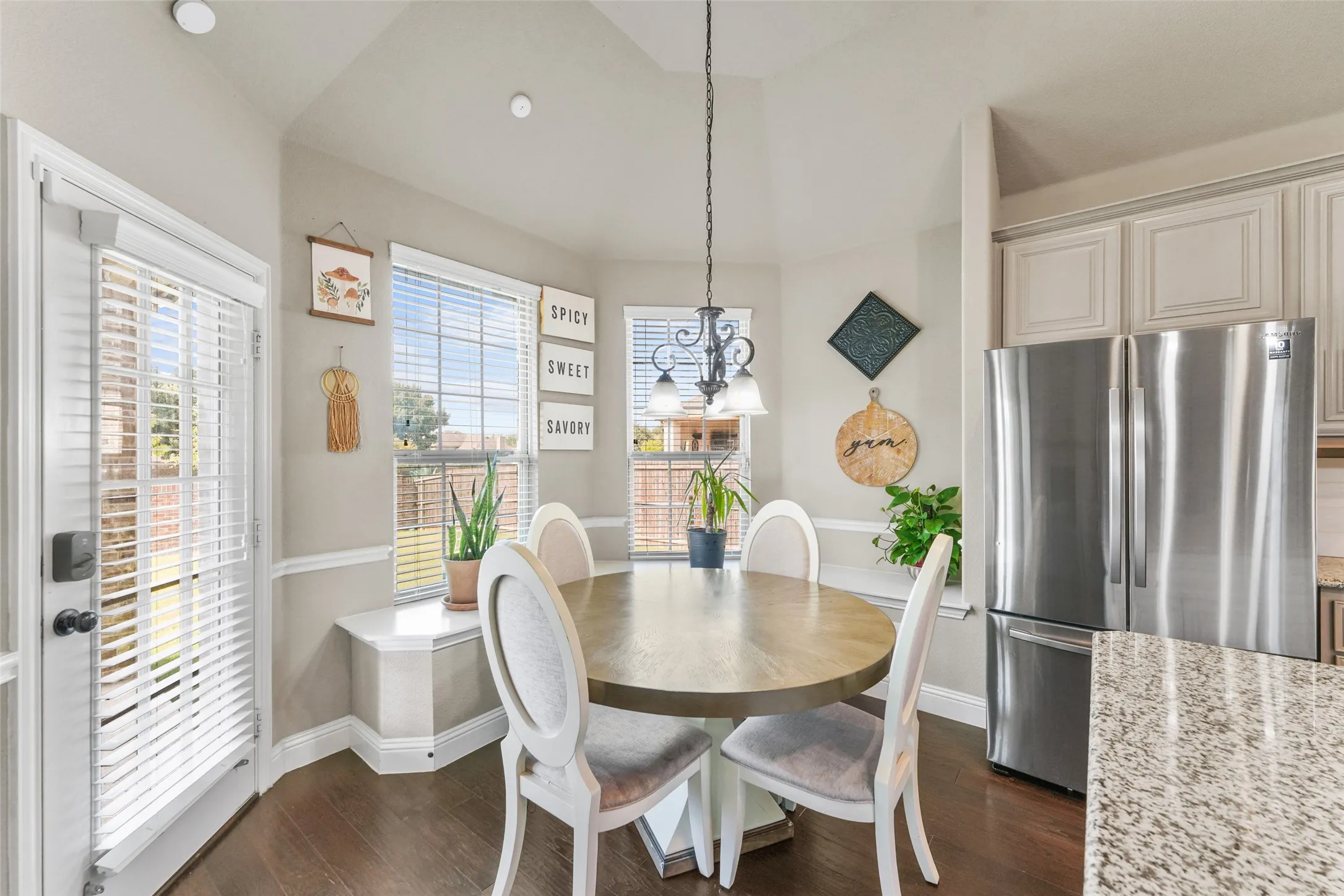 Vaulted ceilings, wood-finish flooring, bay window with built-in bench, stainless steel French door refrigerator, and recessed lighting