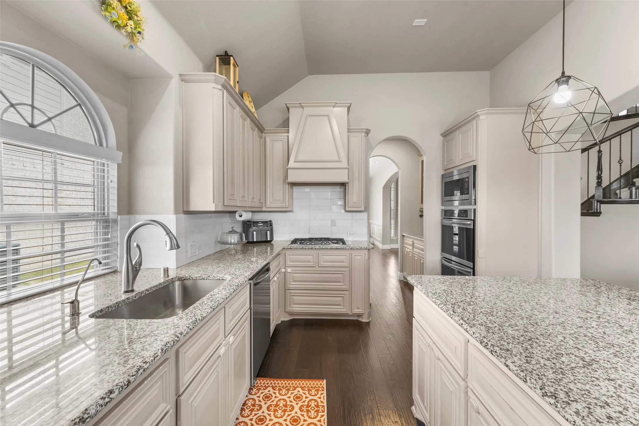 Kitchen featuring light-toned cabinetry, granite countertops, stainless steel appliances, a white tile backsplash, and wood-finish flooring
