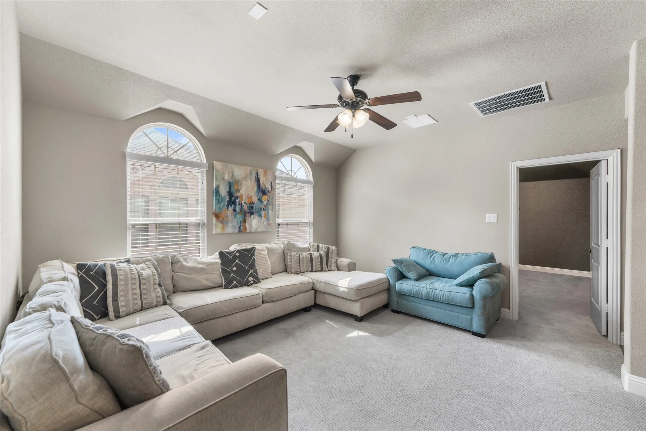 Arched windows with blinds, light gray carpeting, ceiling fan with integrated lighting, and a white paneled door