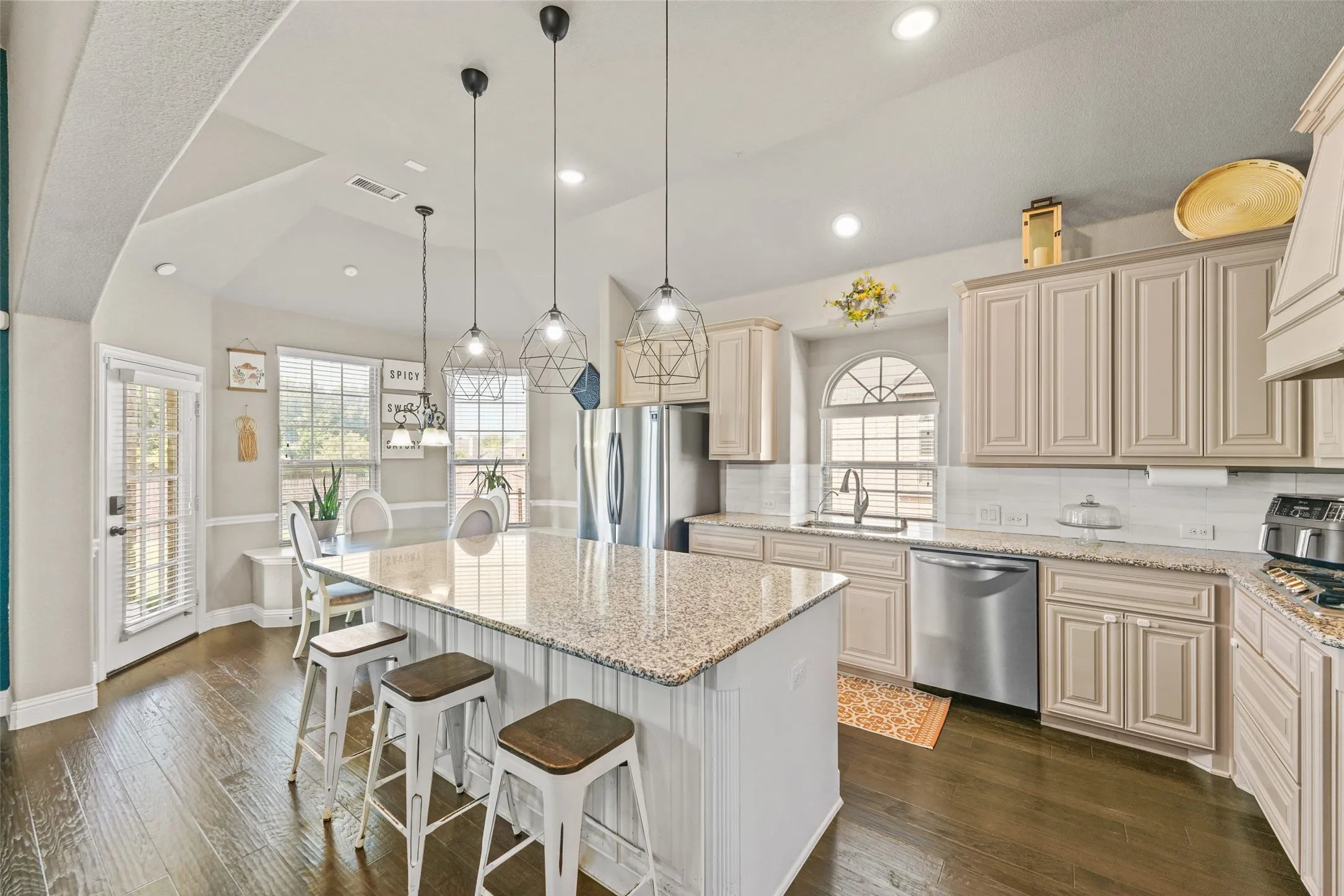Kitchen featuring vaulted ceilings, wood-finish flooring, a central island with a granite countertop, pendant lighting, and stainless steel appliances