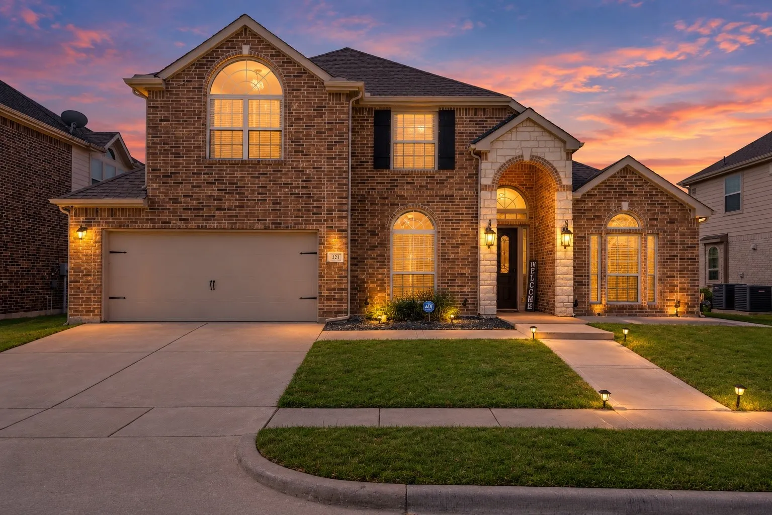 Brick facade with stone accents, arched entryway, attached garage, well-maintained lawn, and a concrete driveway