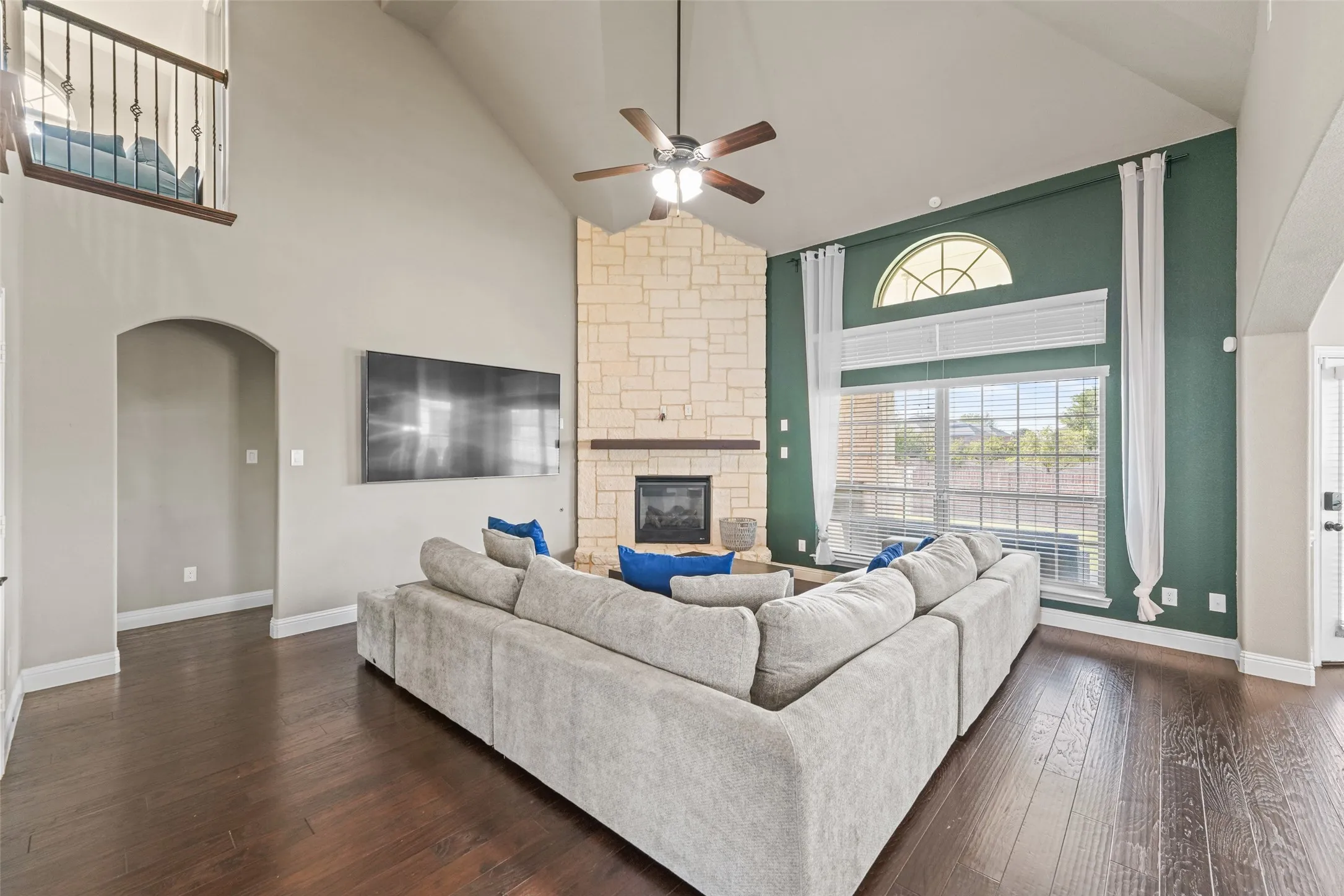Spacious great room featuring soaring vaulted ceilings with ceiling fan, wood-finish flooring throughout, and a fireplace with tile surround