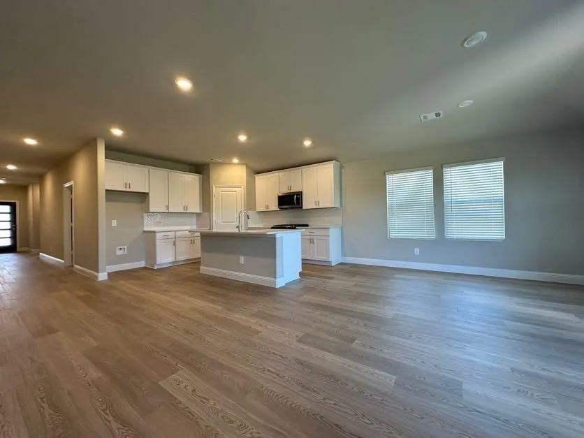 Expansive open-concept living area featuring wood-finish flooring, recessed lighting, and a kitchen with white cabinetry, a central island, and a tile backsplash
