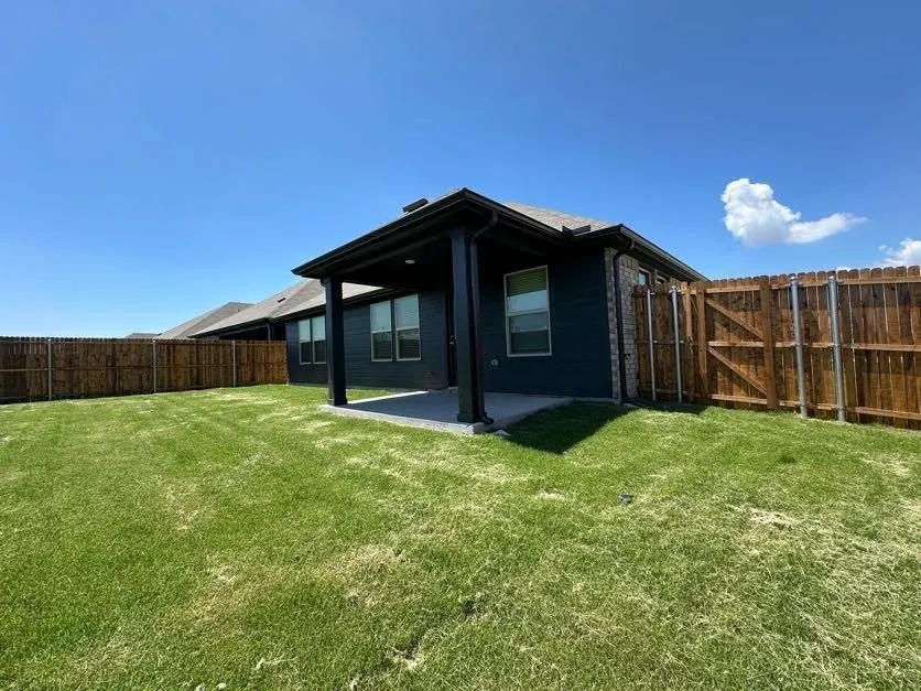 Expansive backyard featuring a covered patio, wood privacy fence, and manicured lawn
