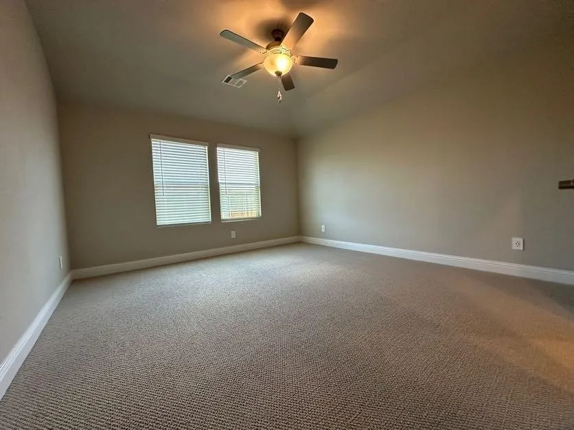 Vaulted ceiling with a ceiling fan, dual windows with blinds, neutral carpeting, and light-toned wall paint