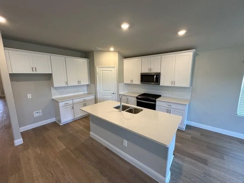 Kitchen featuring white cabinetry, light-toned countertops, a center island with a double basin sink, wood-finish flooring, and recessed lighting