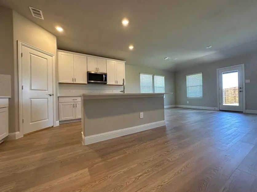 Spacious open-concept living area with wood-finish flooring, recessed lighting, and a kitchen featuring white cabinetry, a built-in microwave, and a breakfast bar