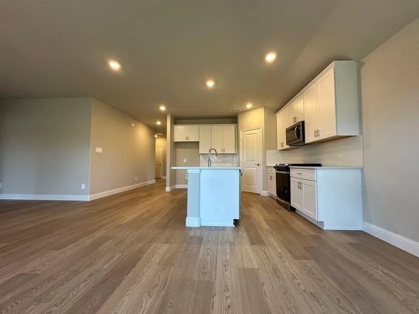 Open-concept layout with wood-finish flooring, recessed lighting, white kitchen cabinetry, and a central island with a sink