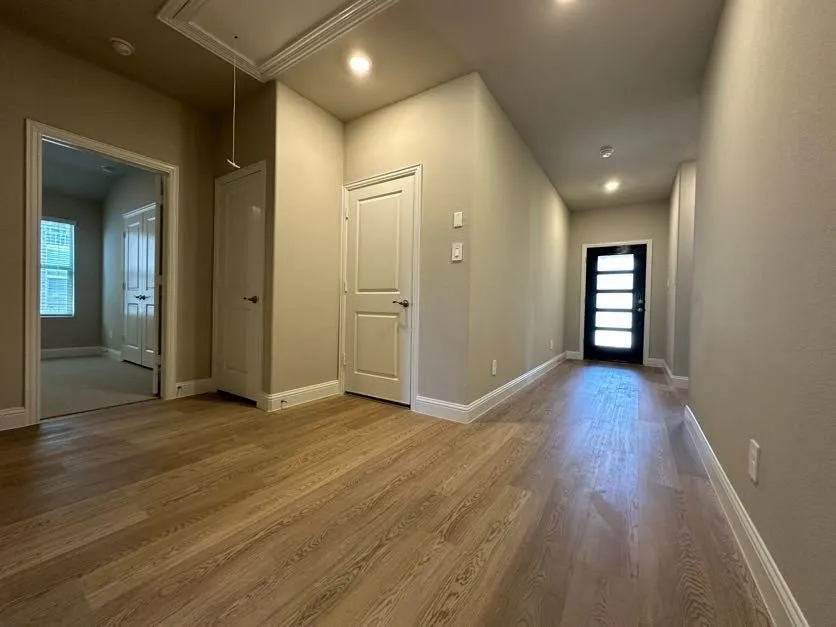 Light wood-finish flooring, recessed ceiling lighting, a contemporary front door with horizontal lites, and crisp white trim