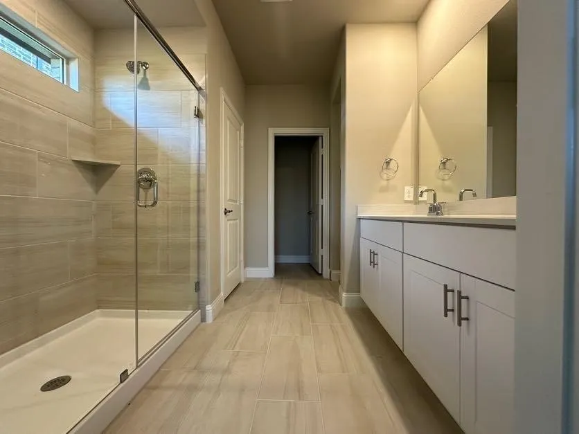 Bathroom featuring a walk-in shower with glass enclosure, integrated shower niche, and a dual-sink vanity with white cabinetry and chrome hardware