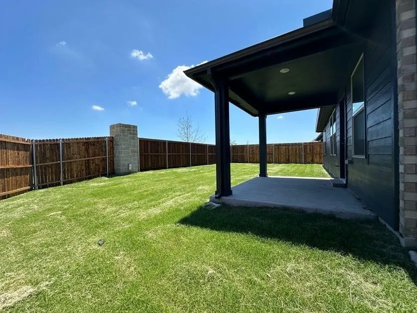 Expansive backyard featuring a manicured lawn, a covered patio, privacy fencing, and brick veneer siding
