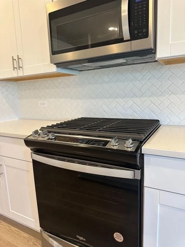 Stainless steel microwave, white shaker cabinetry, white herringbone tile backsplash, and dark finish range with stainless steel accents