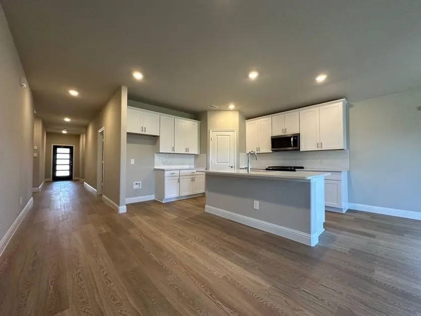 Wood-finish flooring, recessed lighting, white shaker-style cabinetry, and a kitchen island with an integrated sink