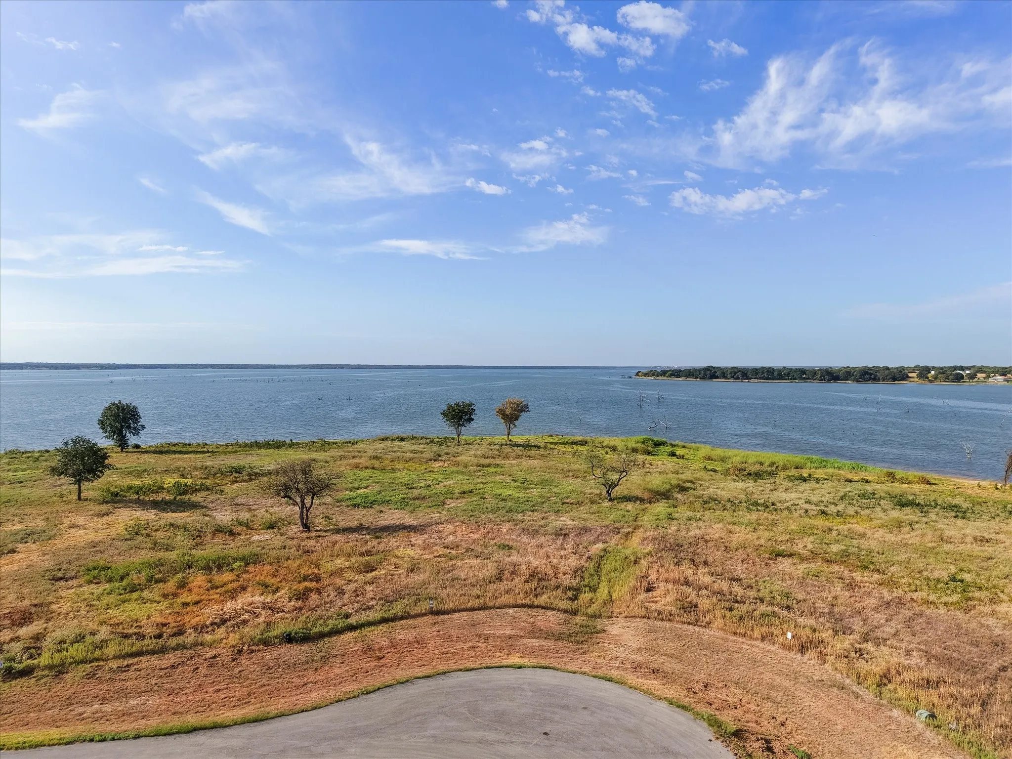 Expansive waterfront property featuring a wide body of water, natural terrain, and scattered trees