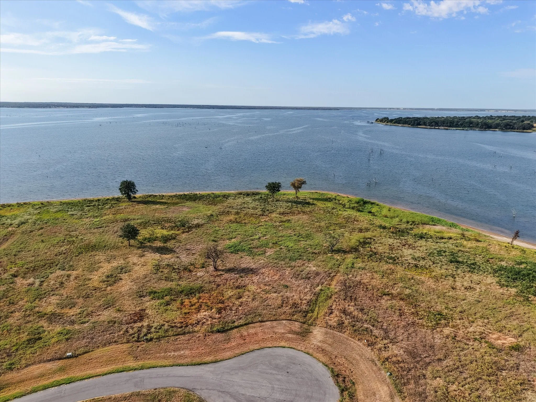 Expansive waterfront property featuring a clear body of water, natural terrain, and a paved road