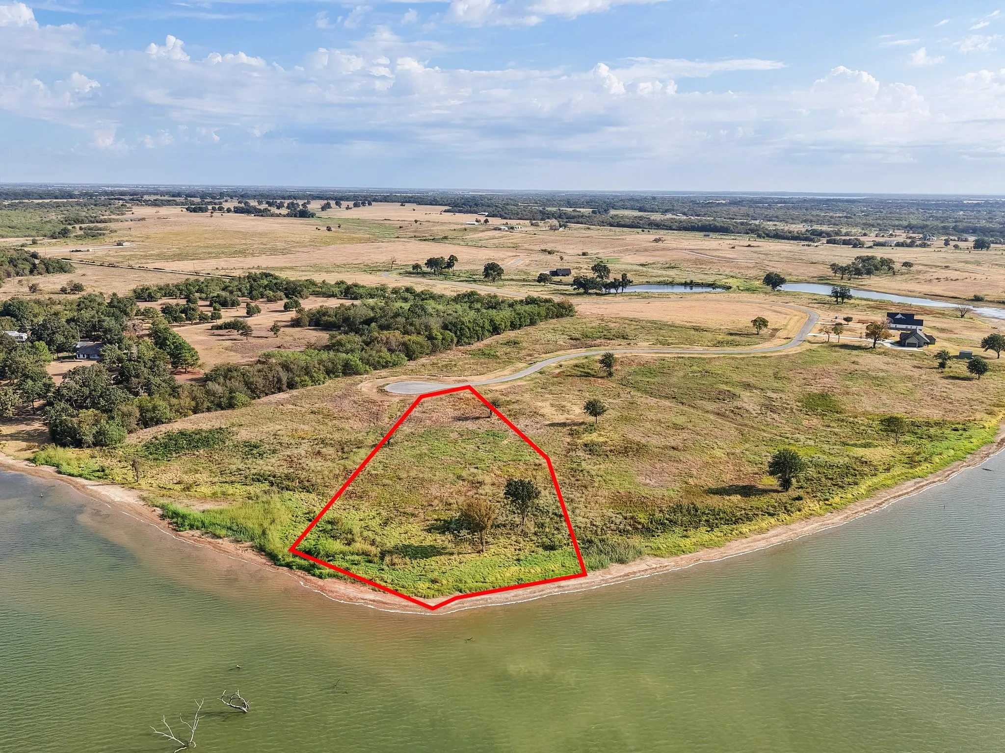 Waterfront property with a natural shoreline, featuring open land, scattered trees, and a distant water body