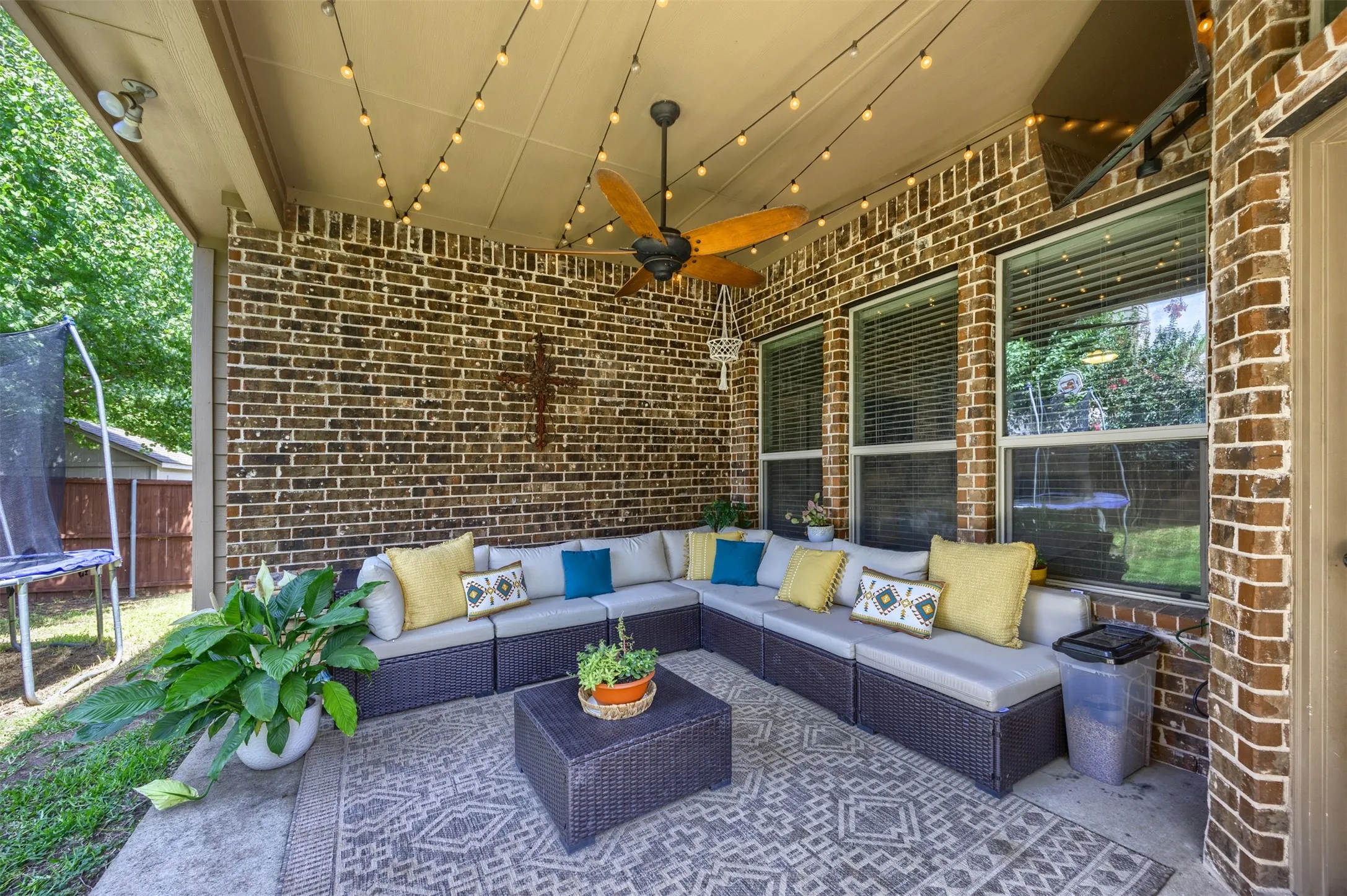 “Covered patio with ceiling fan and café lighting extends the living space outdoors beneath mature shade trees