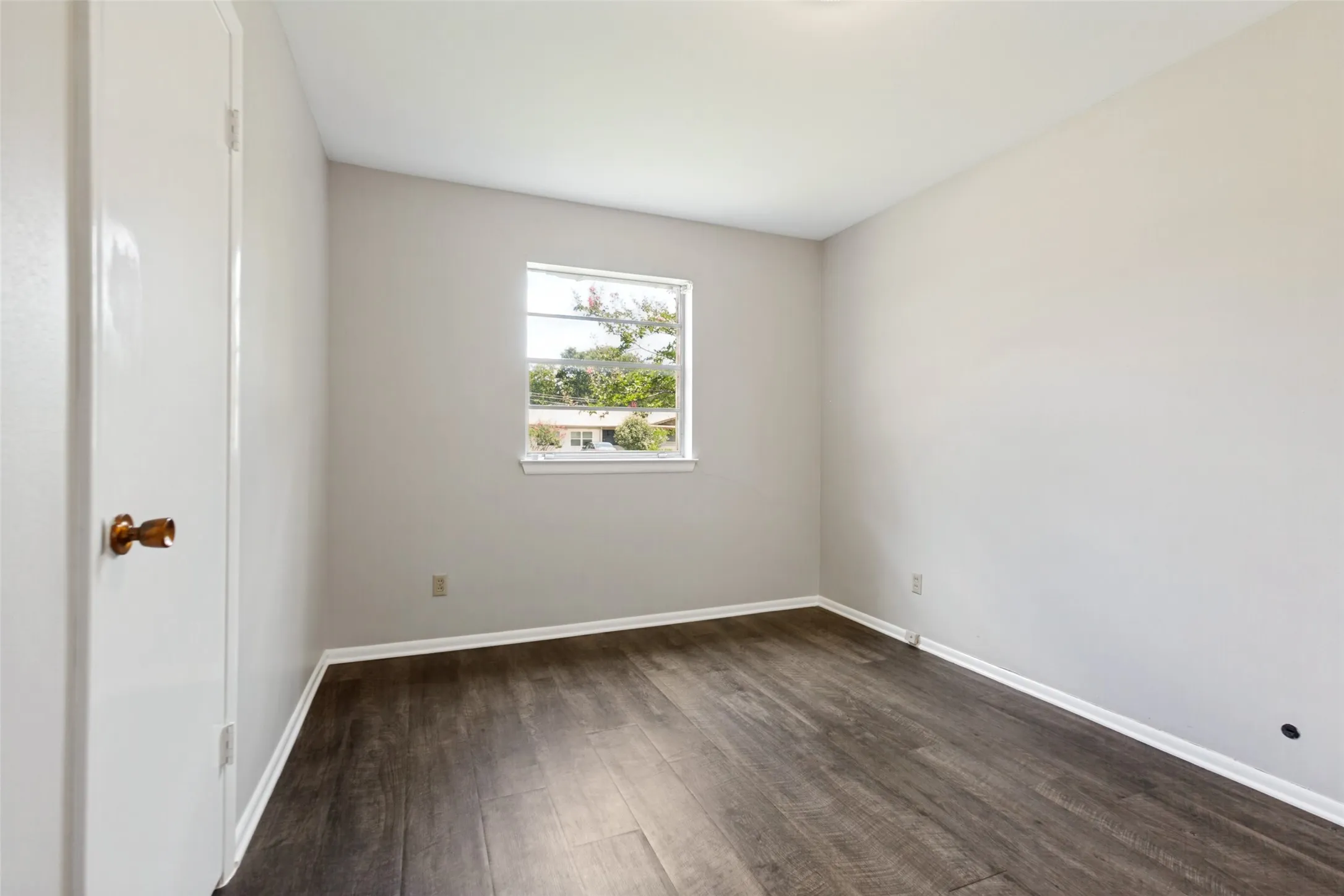 Wood-finish flooring with white trim, light gray walls, and a white door with a brass-finish knob