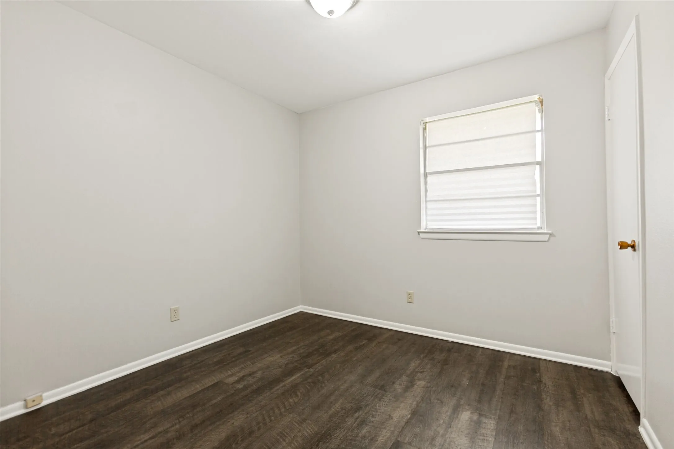 Wood-finish flooring, white walls, and a window with blinds